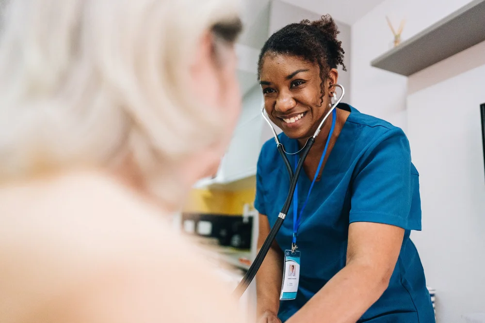 A caregiver in scrubs smiling while helping an older client