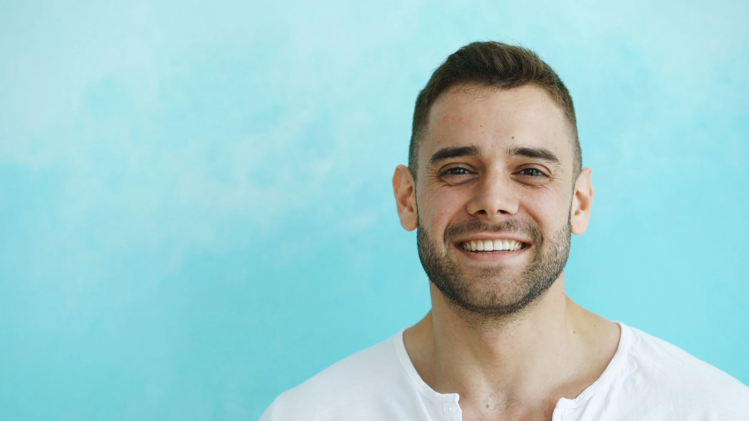 Smiling man with a beard in front of a teal background