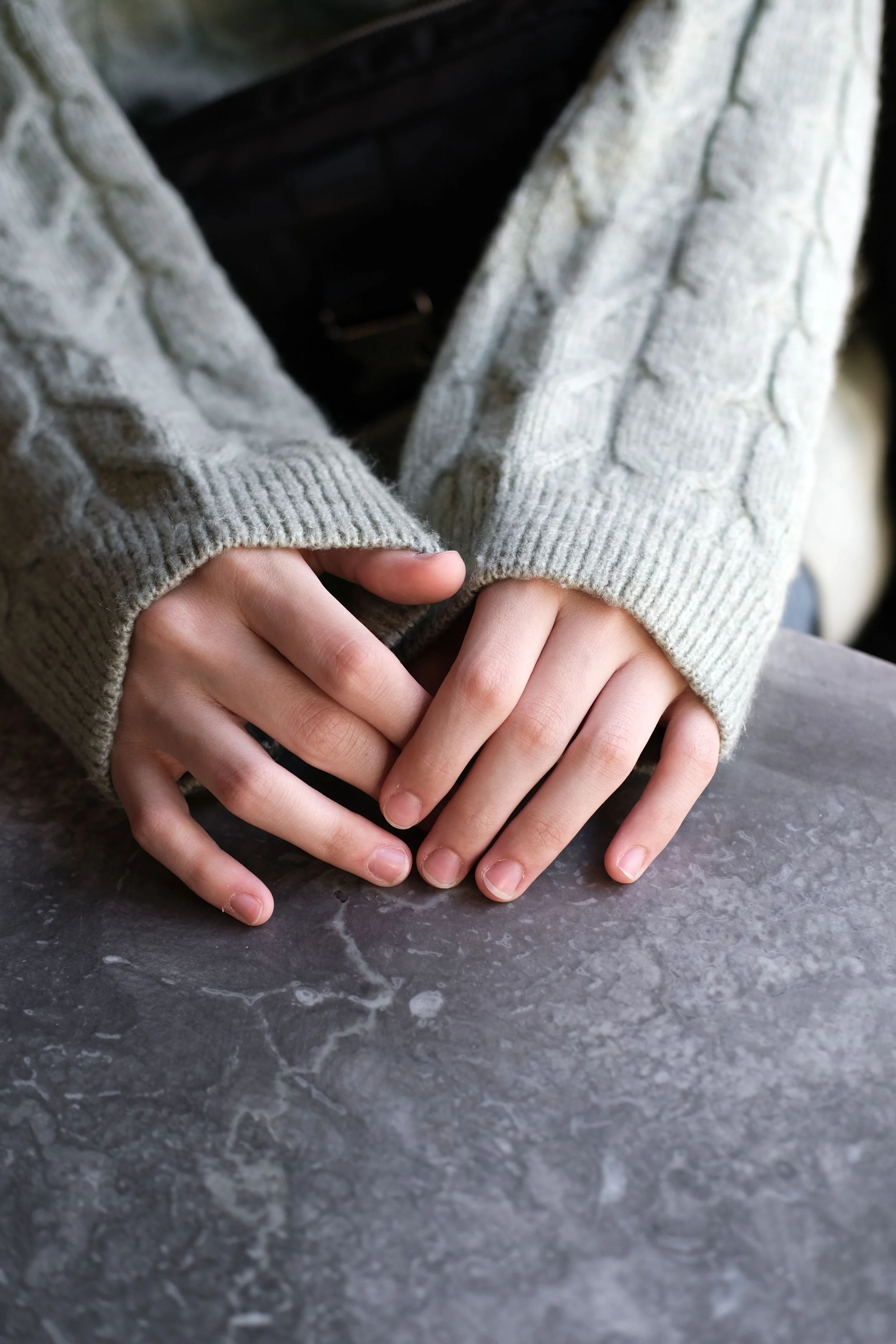 Child's hands in a knit sweater resting on a stone surface