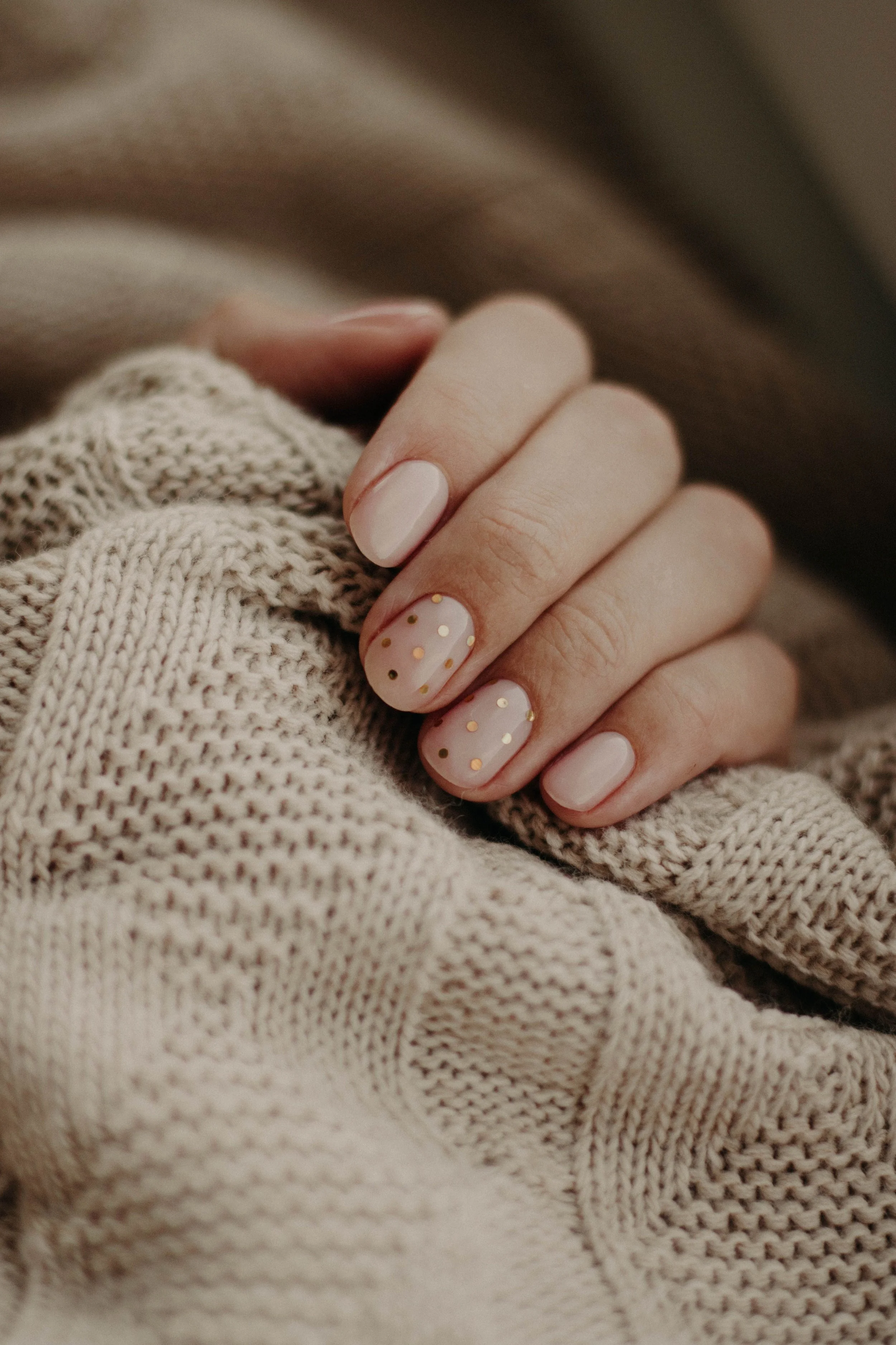 Woman's nails painted with gold glitter resting on a beige sweater