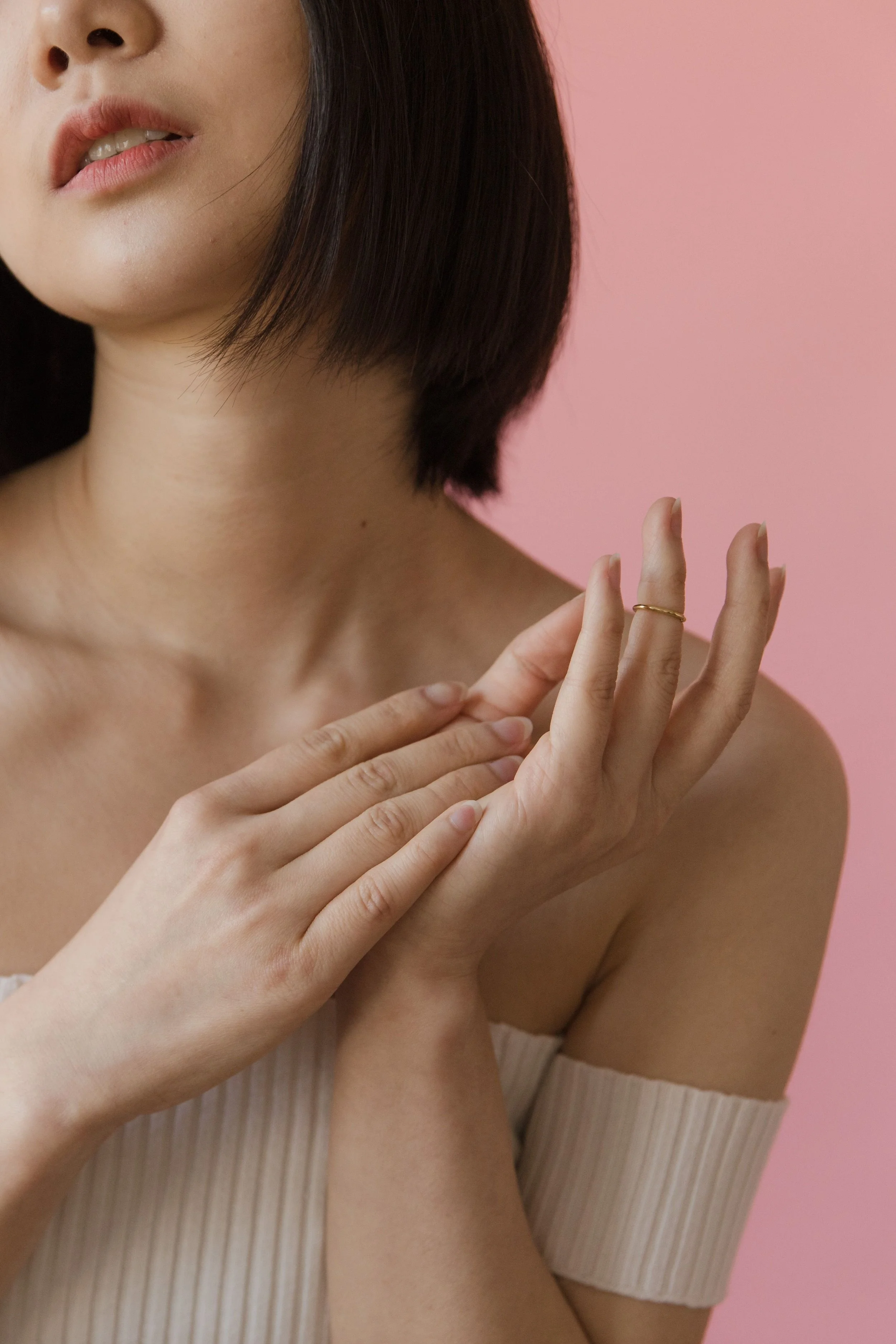 Woman with short black hair touching hands over beige shoulderless top