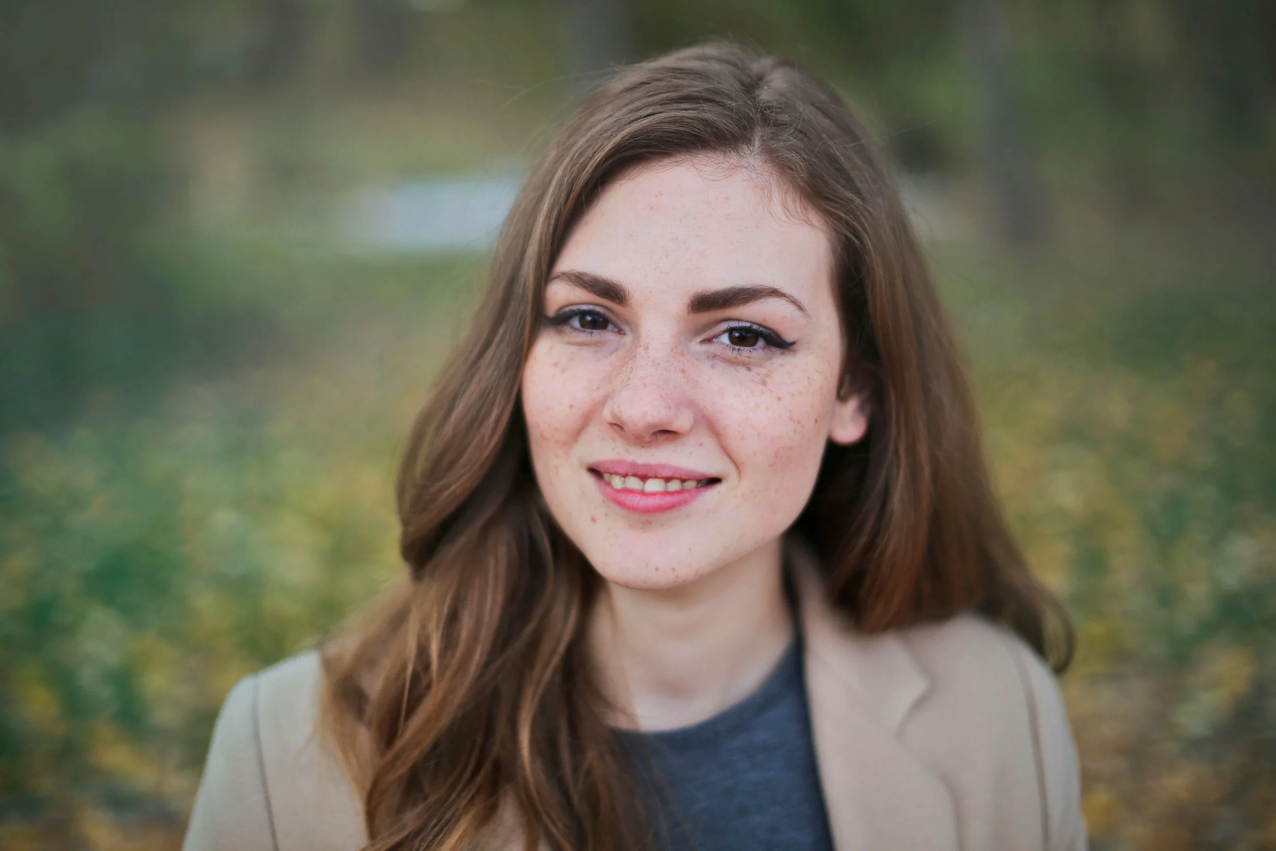 Woman with freckles and long brown hair smiling outdoors