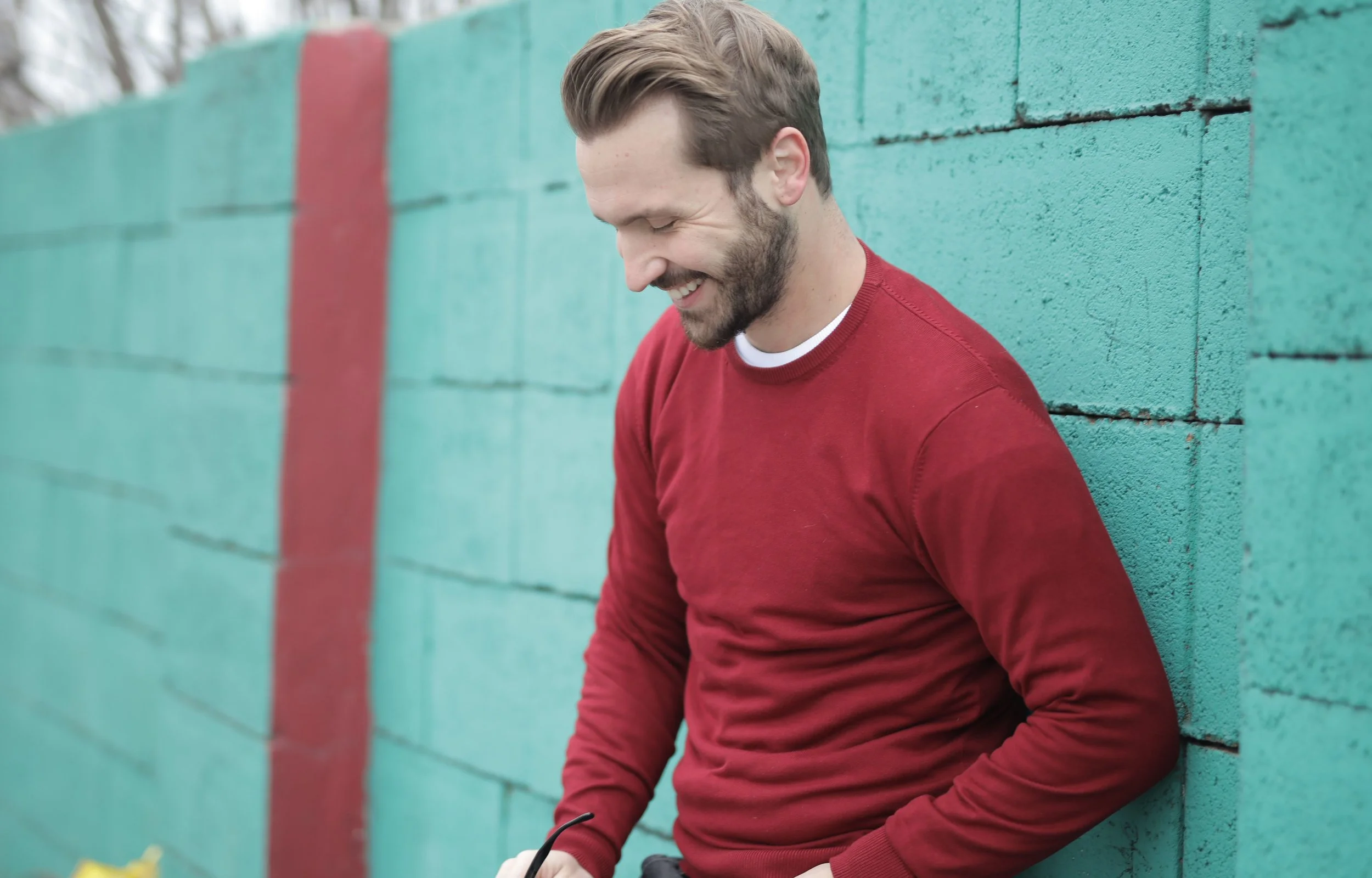 Smiling man in a red sweater leaning against a teal wall