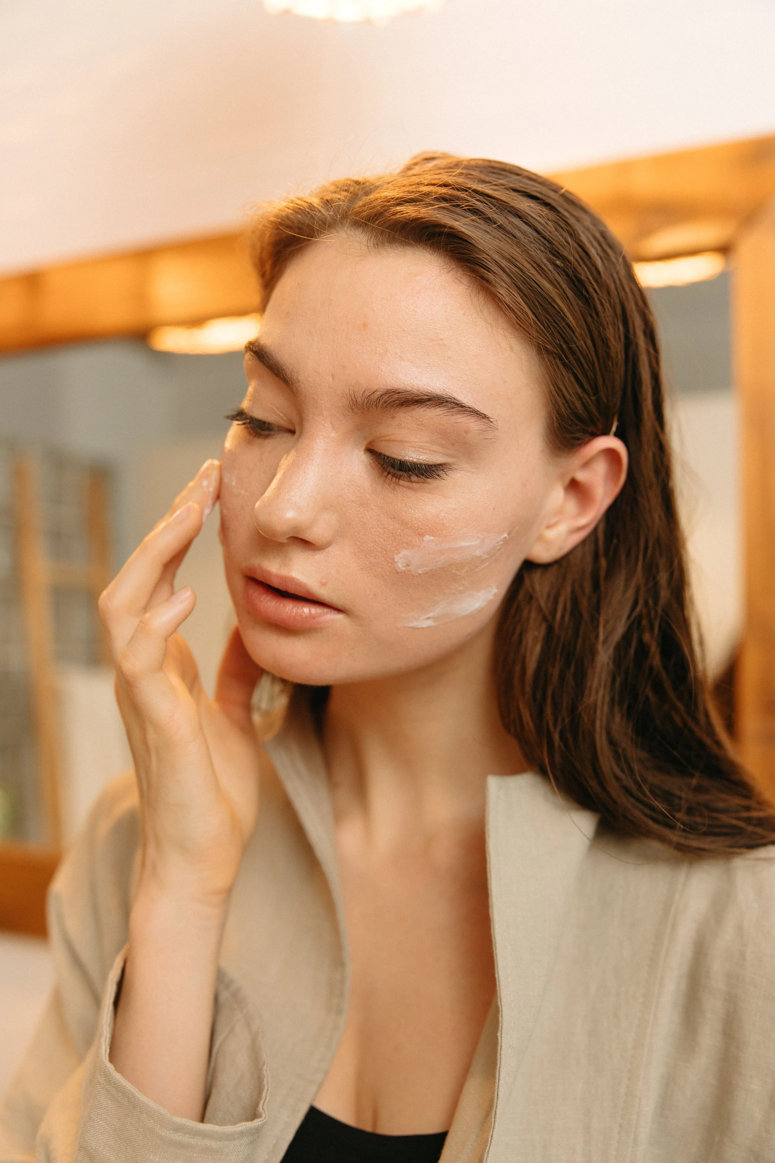Woman in a beige jacket applying cream to her cheek