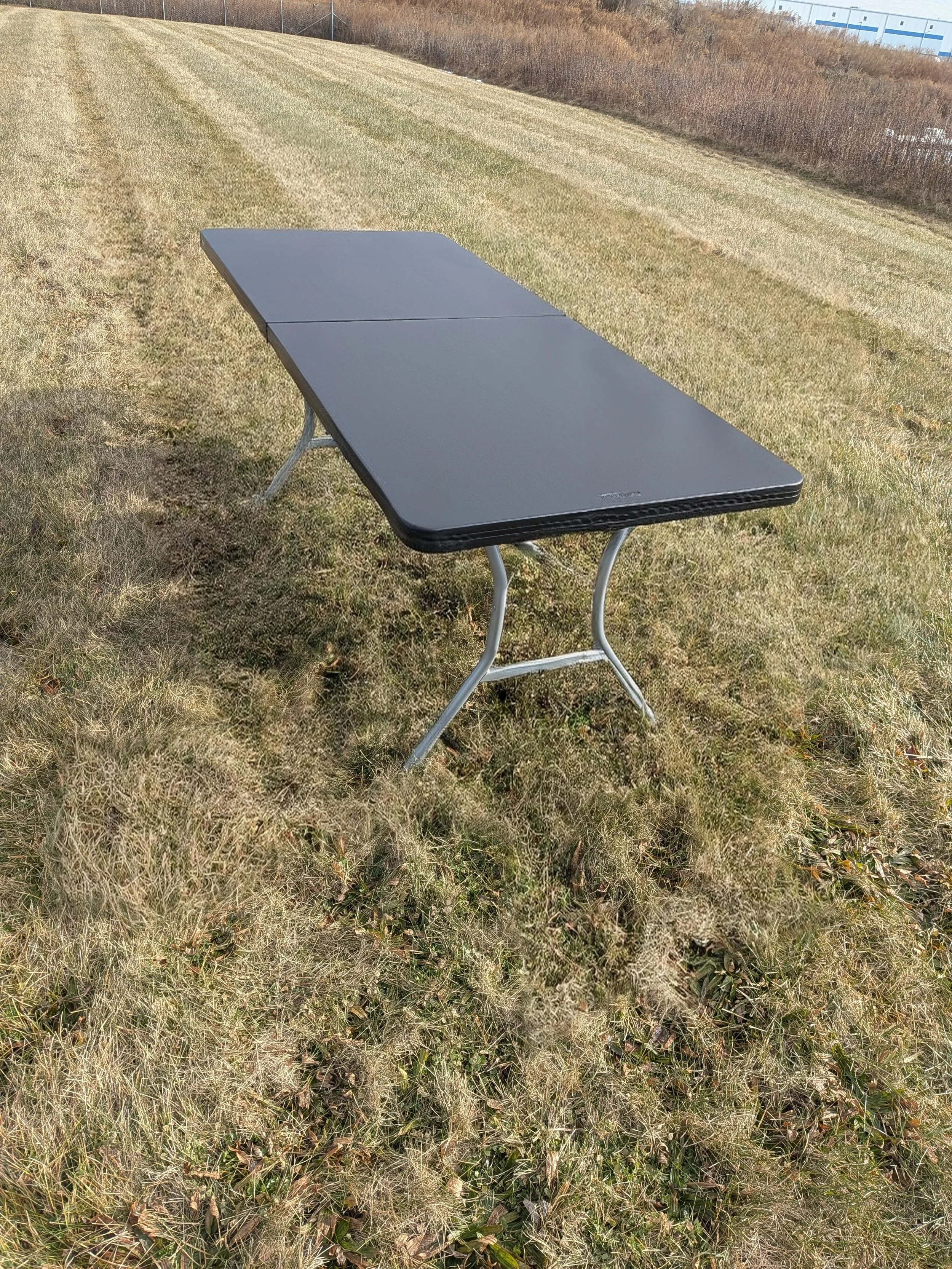 A black portable folding table with aluminum legs standing outdoors on a grassy field.