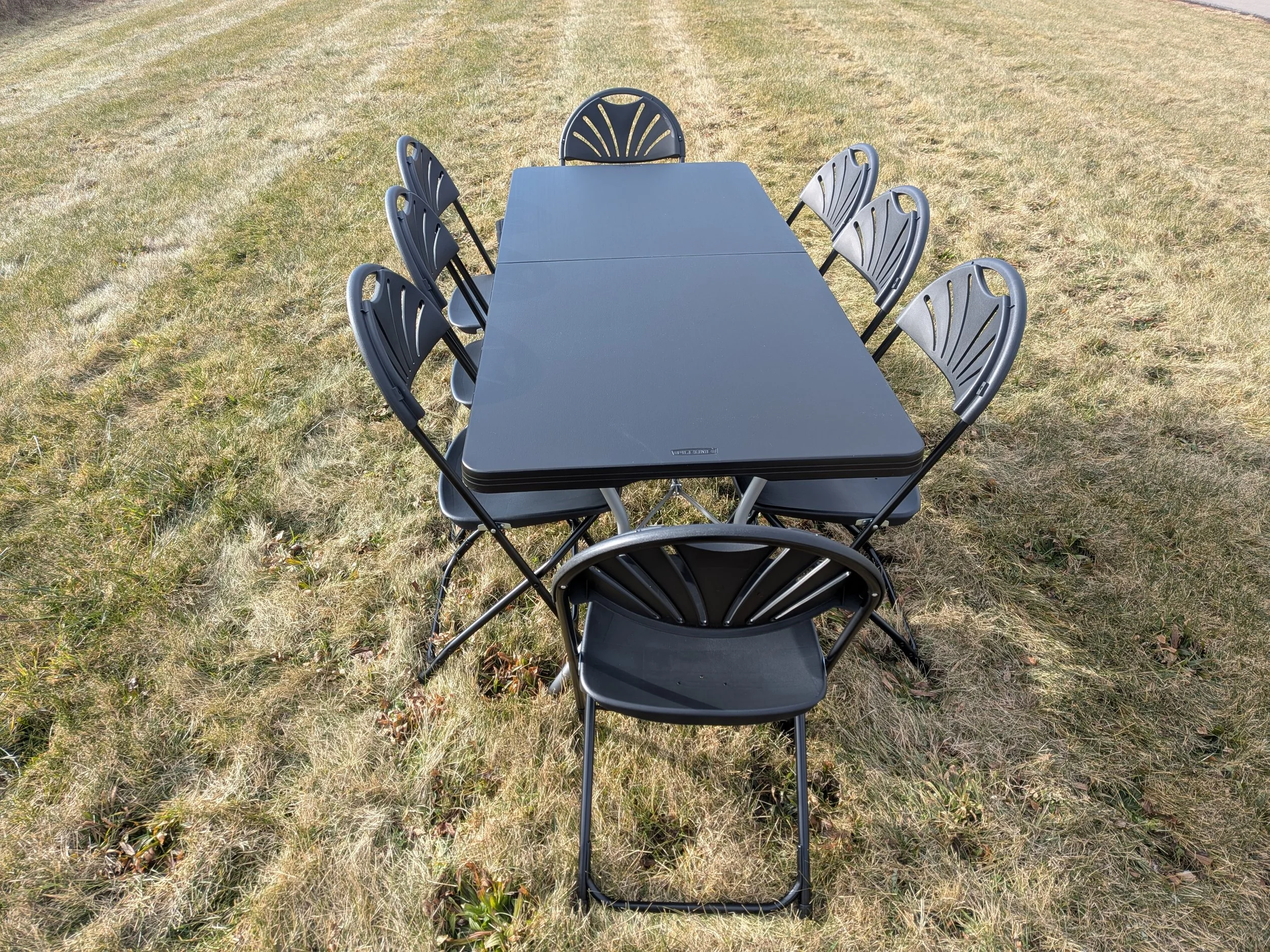 Black outdoor table with eight matching black chairs arranged around it on a grassy lawn.