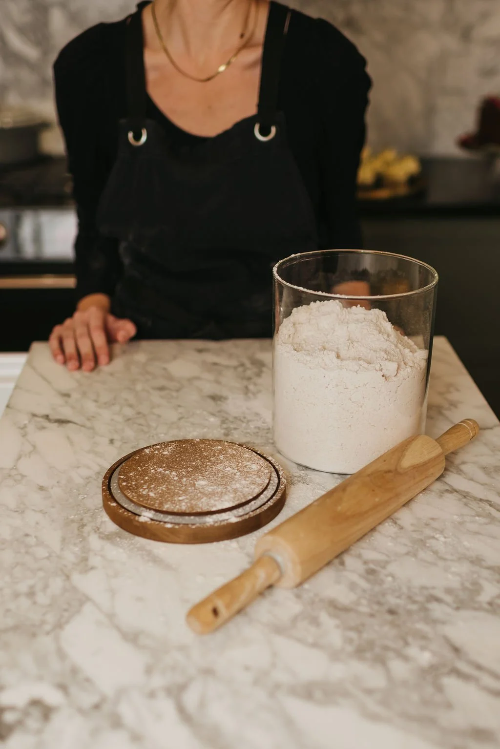 Boutique baker Brittany Bailey at Ember & Bloom Bakery preparing artisan ingredients for a private gluten-free sourdough workshop on a marble countertop.