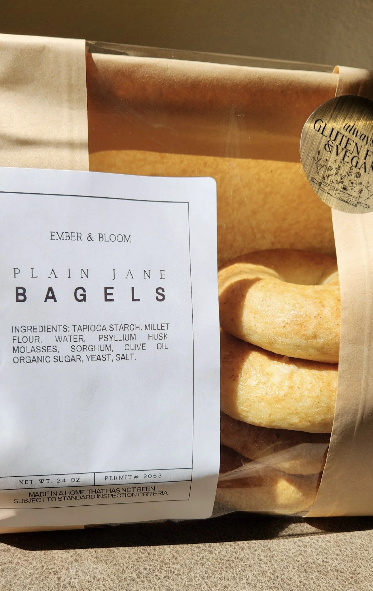 Close-up of Ember & Bloom Plain Jane gluten-free vegan bagels in clear packaging, showing ingredients, net weight, and "always gluten-free & vegan" sticker