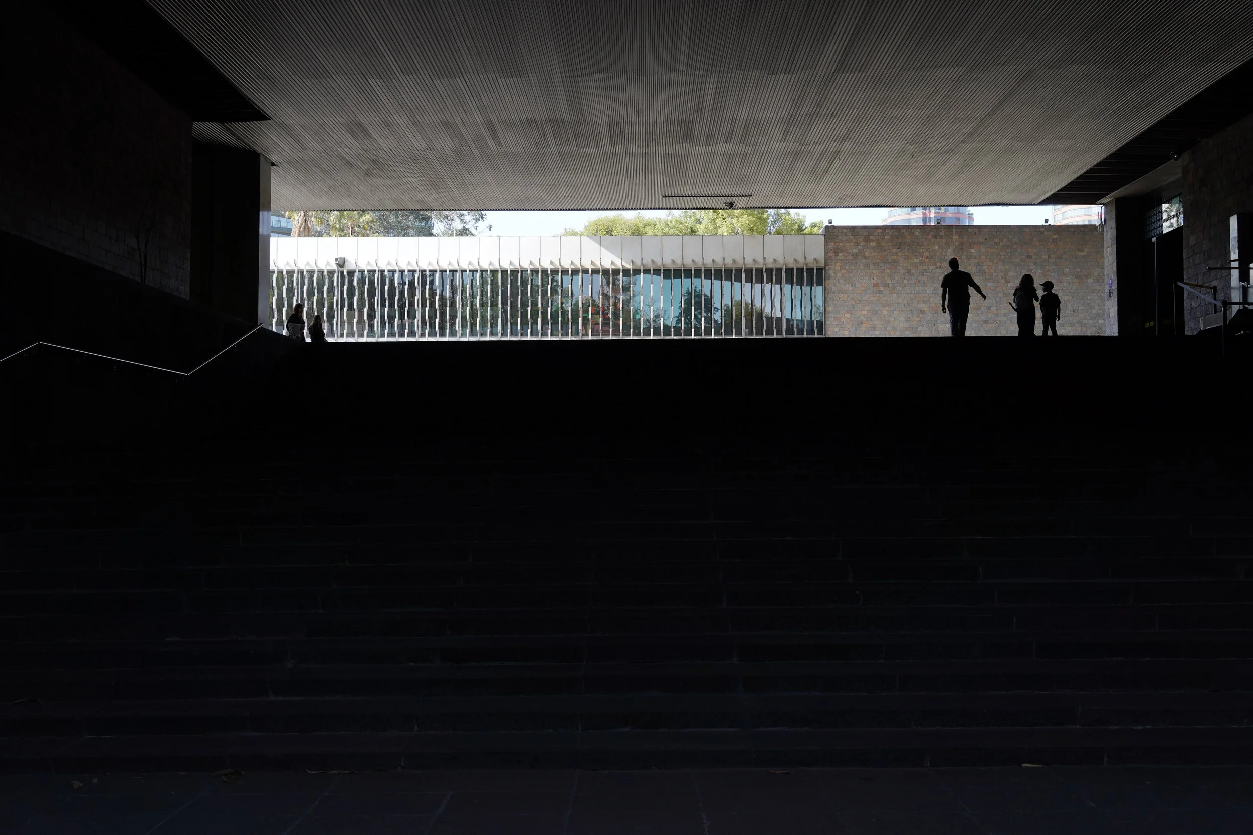 Three figures silhouetted at top of wide steps beneath concrete overhand, Museo Nacional de Antropología, Mexico City, Mexico