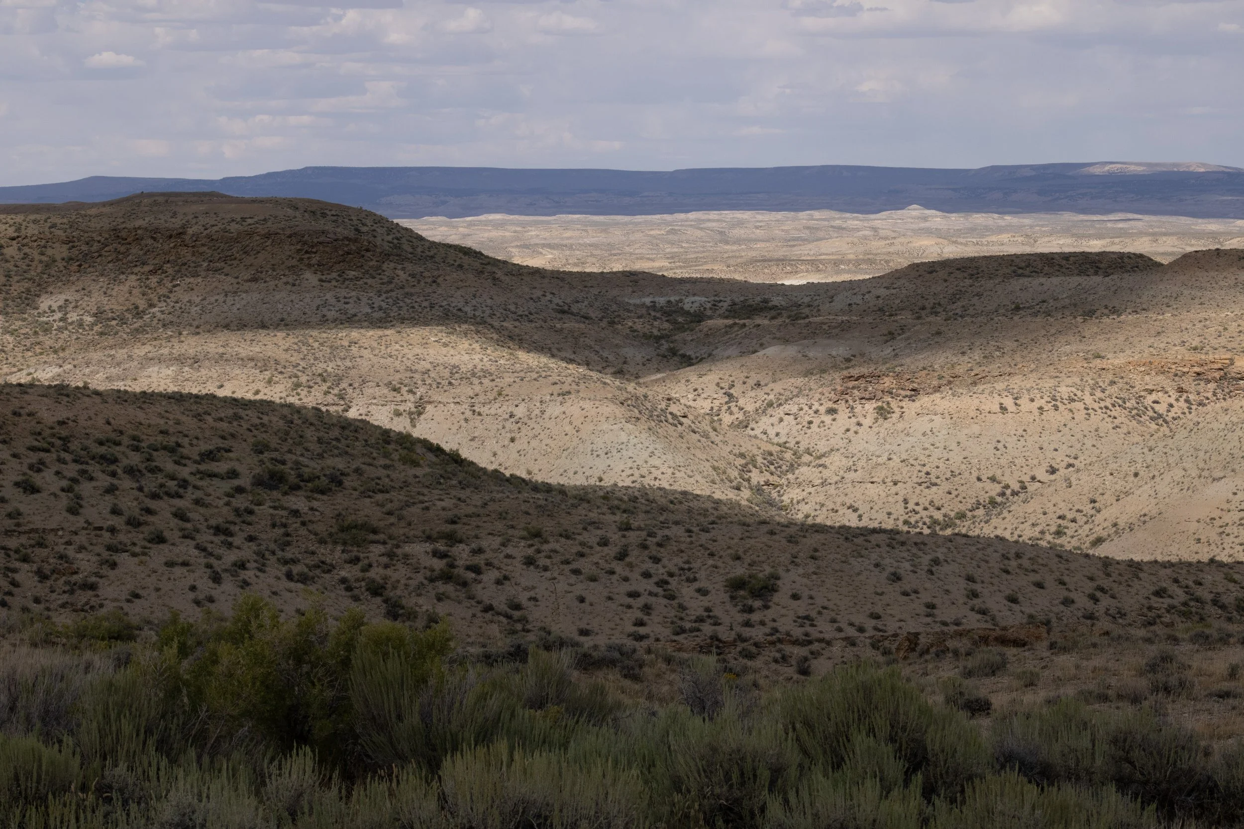 Layered desert hills receding toward a flat mesa on the horizon, Sand Wash Basin, Maybell, CO