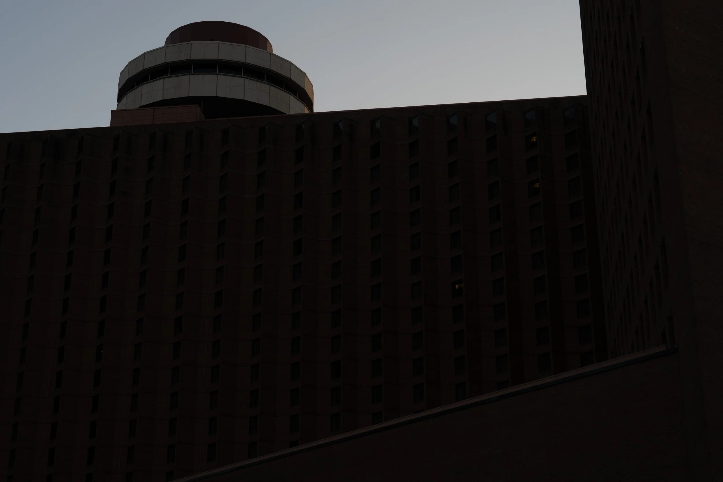Hotel tower facade at twilight, grid of windows in shadow, cylindrical penthouse above, Indianapolis, IN