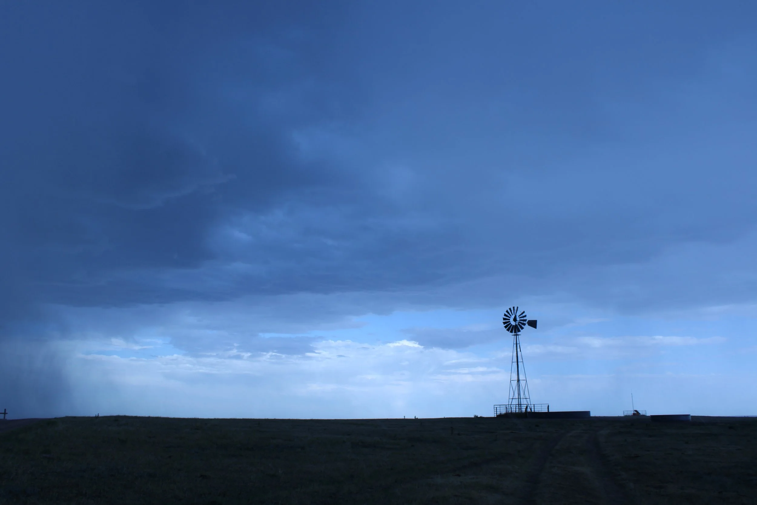 Windmill silhouette on the plains under a stormy blue sky, rain falling on the horizon, Pawnee National Grassland, Ault, CO