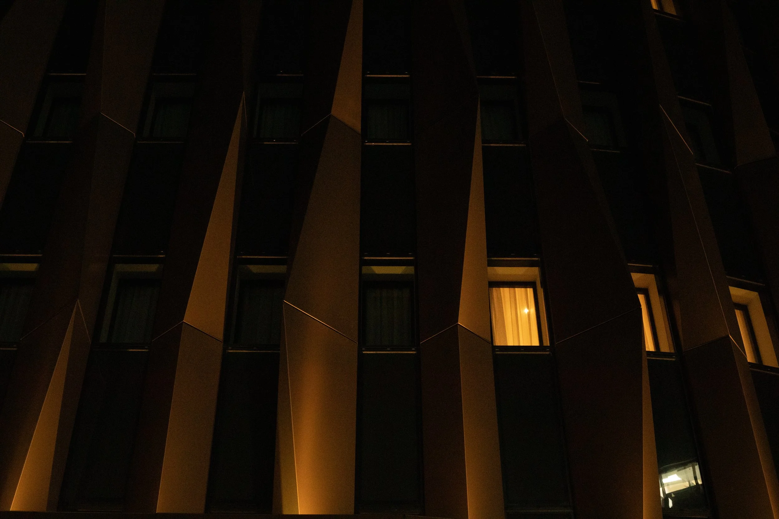 Angled concrete fins on a building facade at night, one room illuminated, London, UK