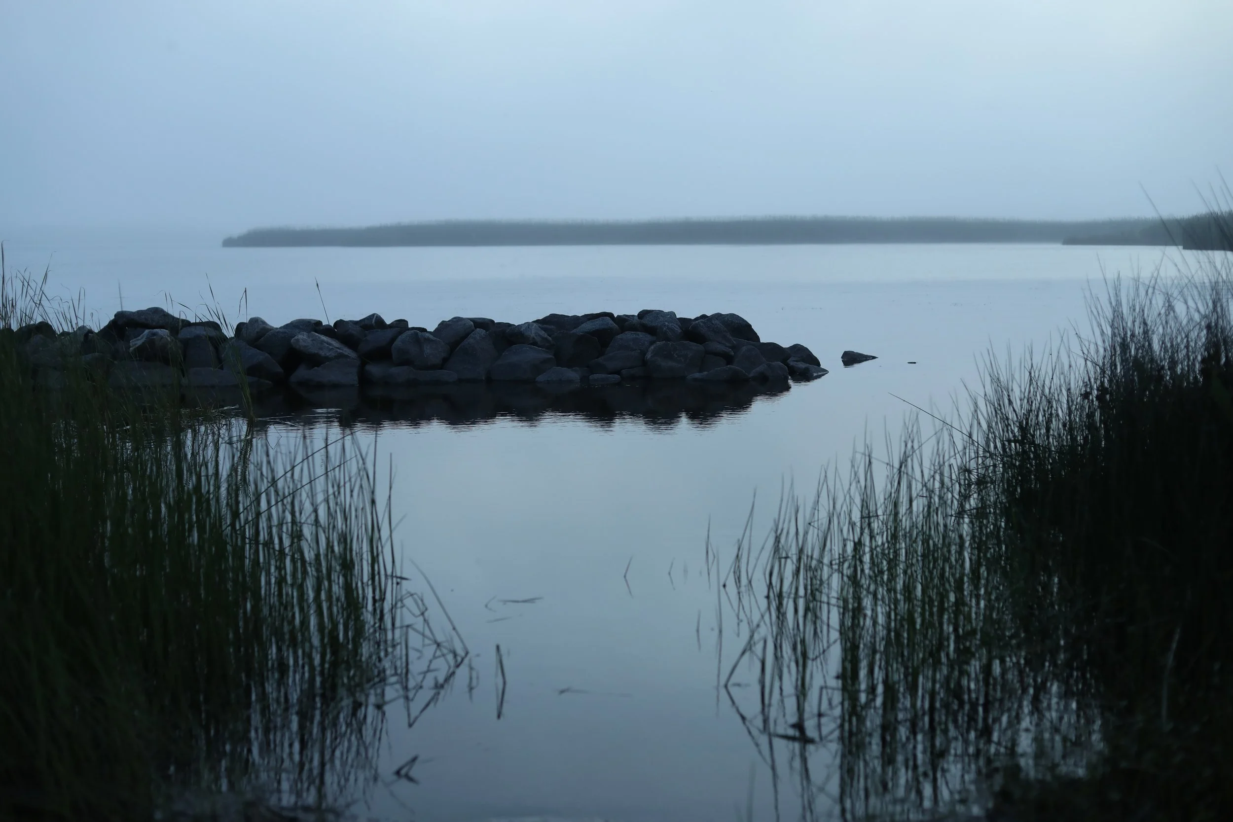 Rock cairn and reeds on a still lake at dusk, fog on the water, Back Bay National Wildlife Refuge, Virginia Beach, VA