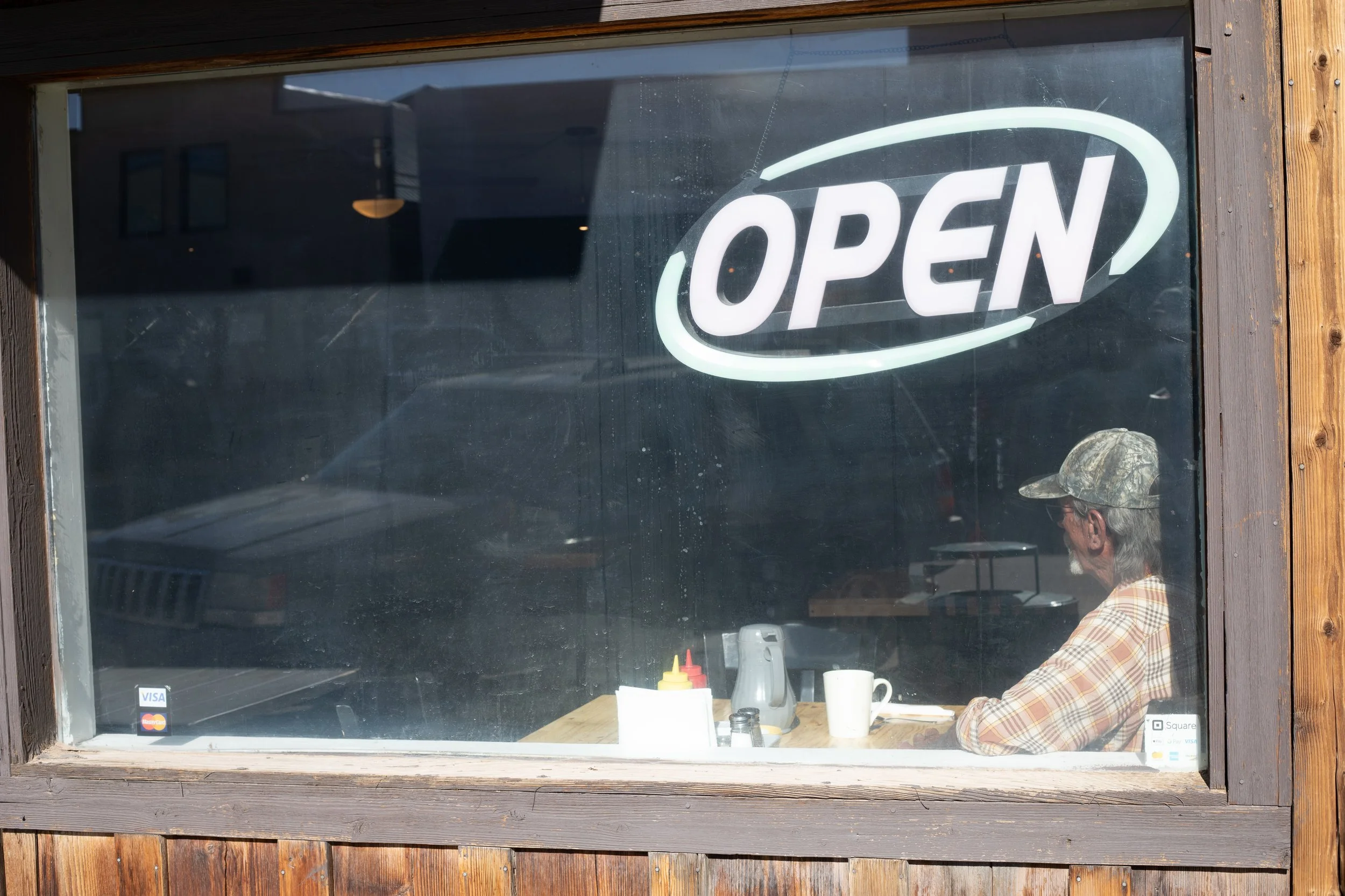 A man sits alone beneath an OPEN sign, Westcliffe, CO
