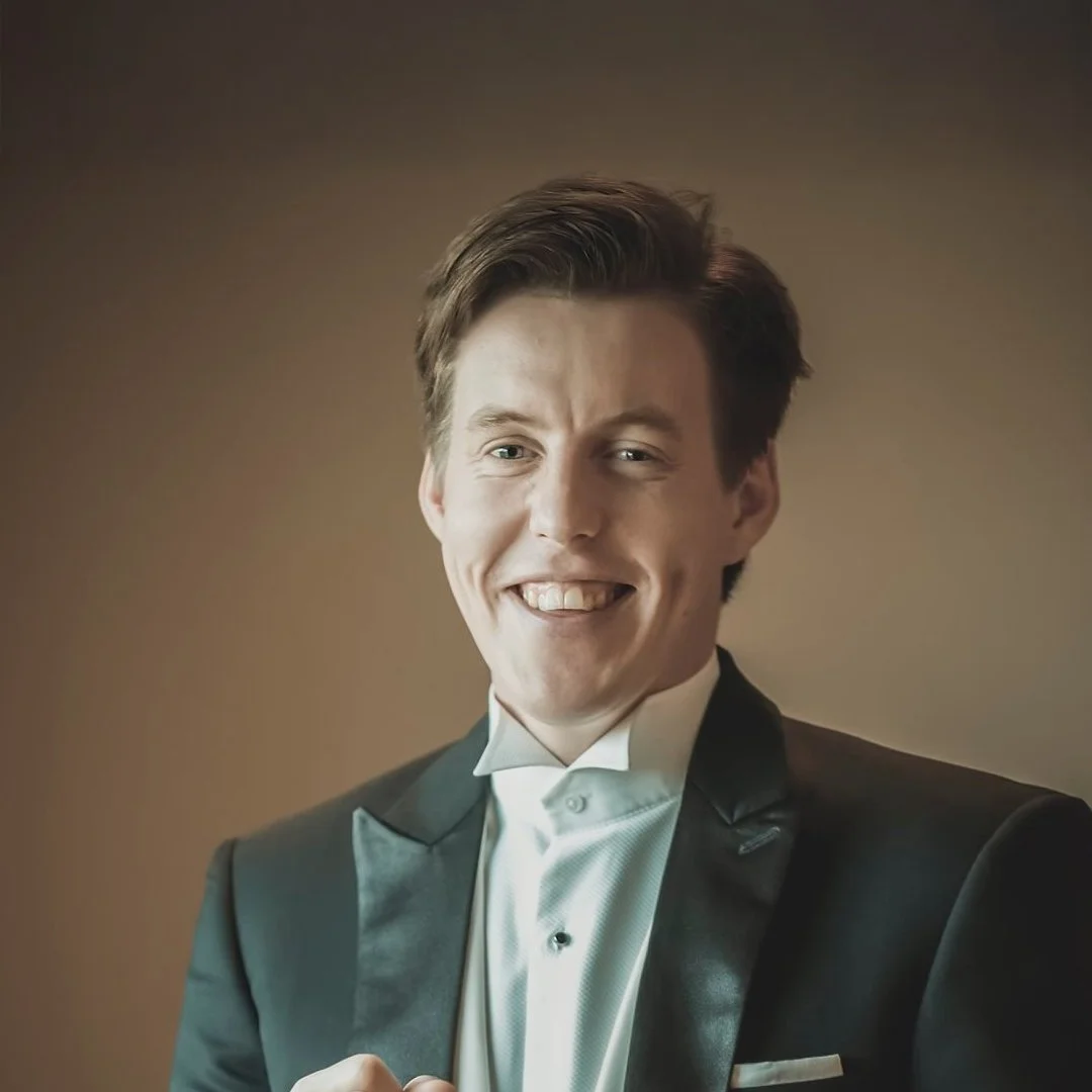 En man i svart kostym och vit skjorta ler mot kameran.