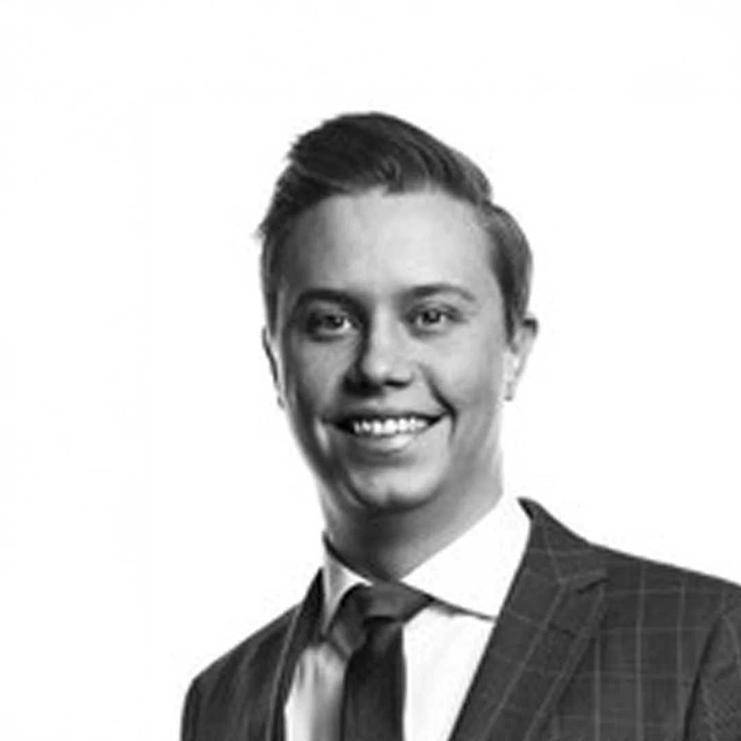 En ung man med herrfrisyr och slips, klädd i kostym, leende mot kameran.