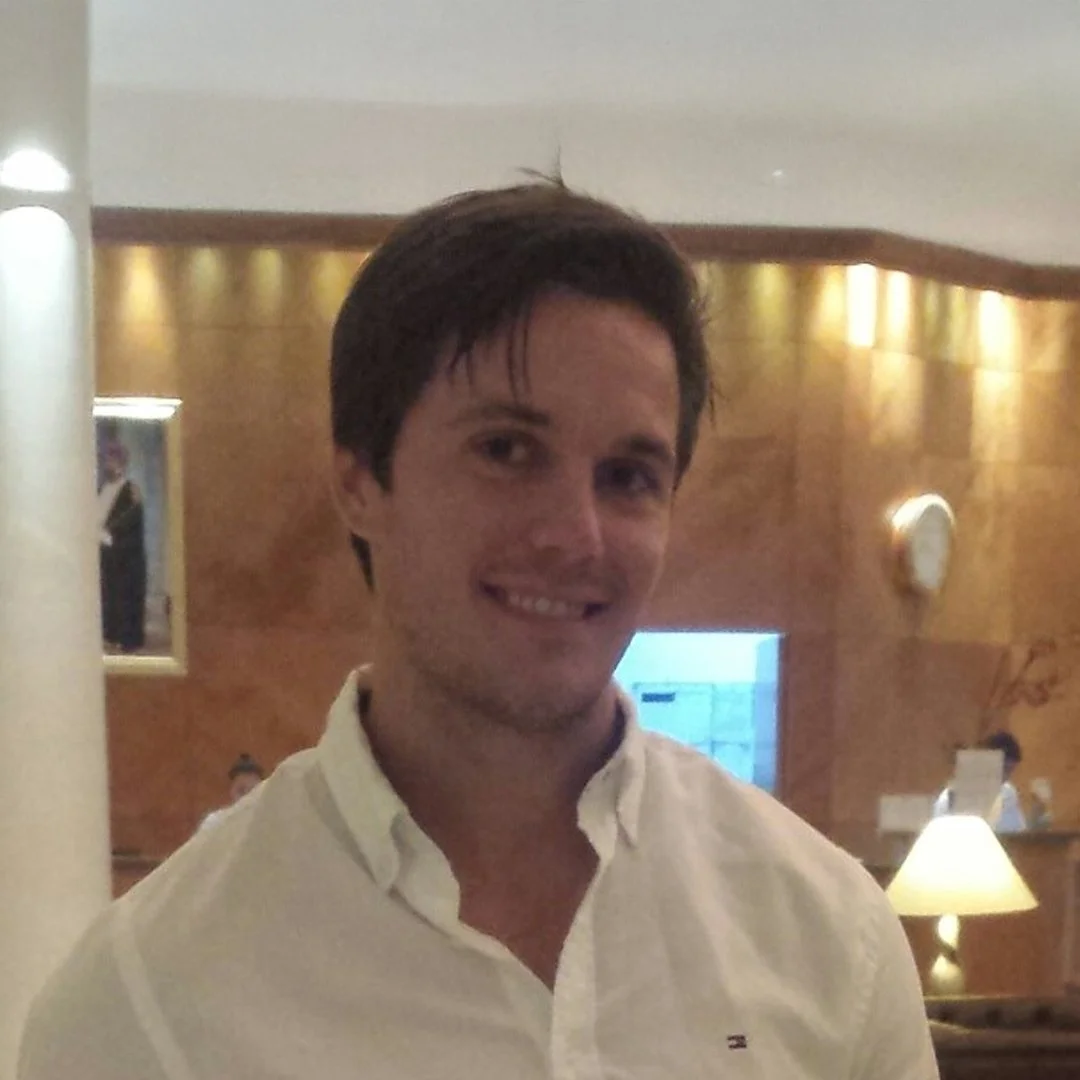 En glad man med mörkt hår, vit skjorta, inomhus i ett varmt belyst rum.