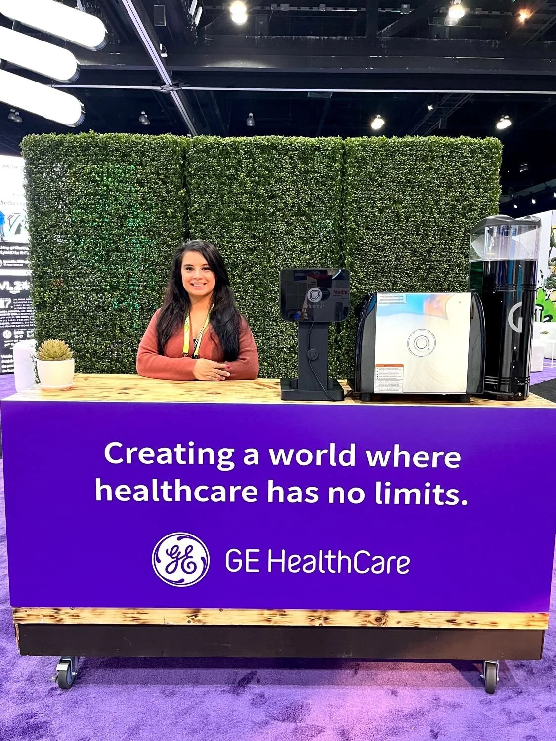 Jodie Lail at VIVE at GE sponsored counter has a purple panel with white text that reads, 'Creating a world where healthcare has no limits,' and the GE Healthcare logo.