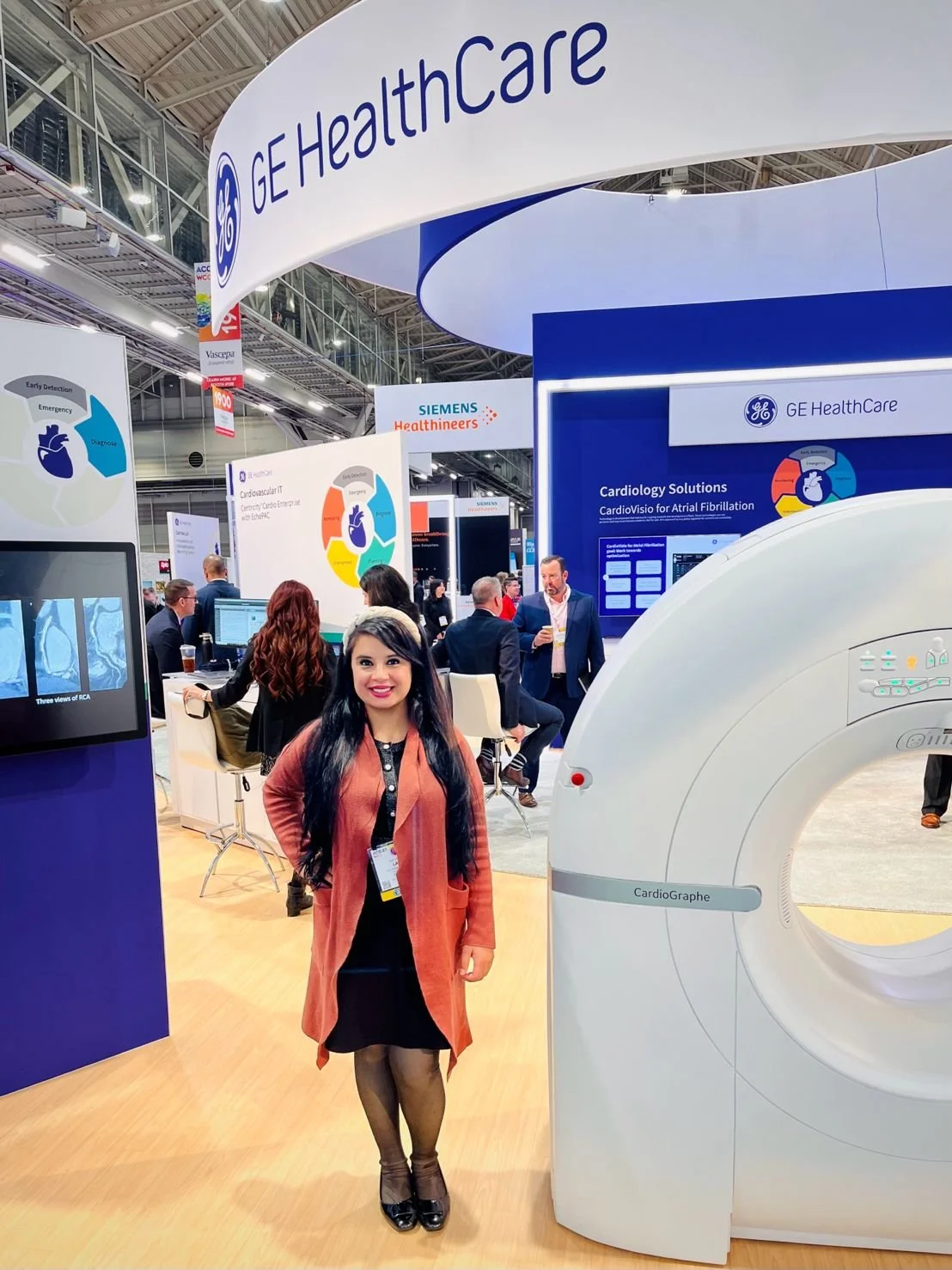 Jodie Lail standing in front of GE Healthcare exhibit at a conference, with medical imaging equipment and other attendees in the background.