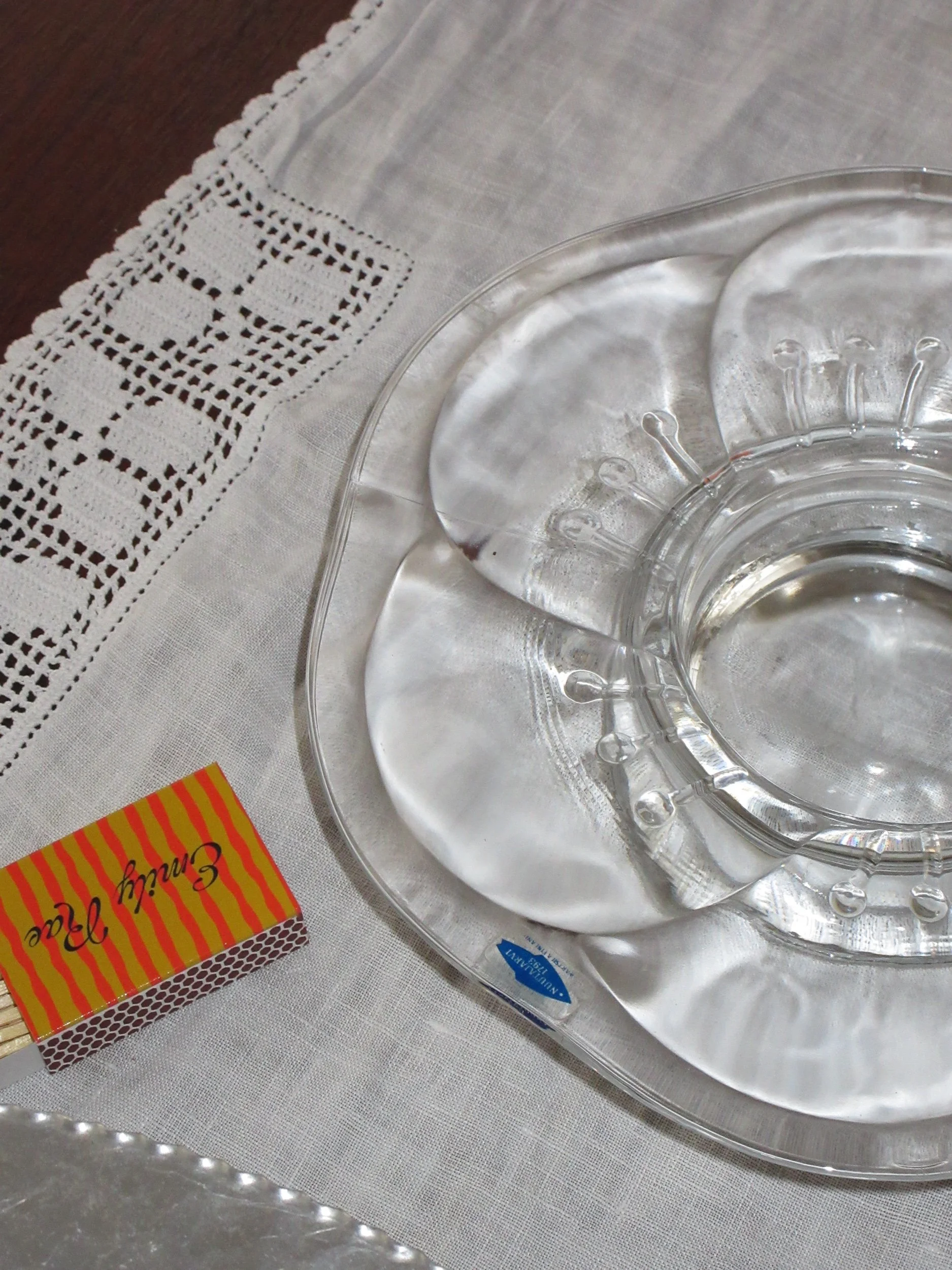 Glass appetizer or dessert dish with two clear glass plates on a white linen tablecloth with lace trim, next to a yellow and red striped matchbox.