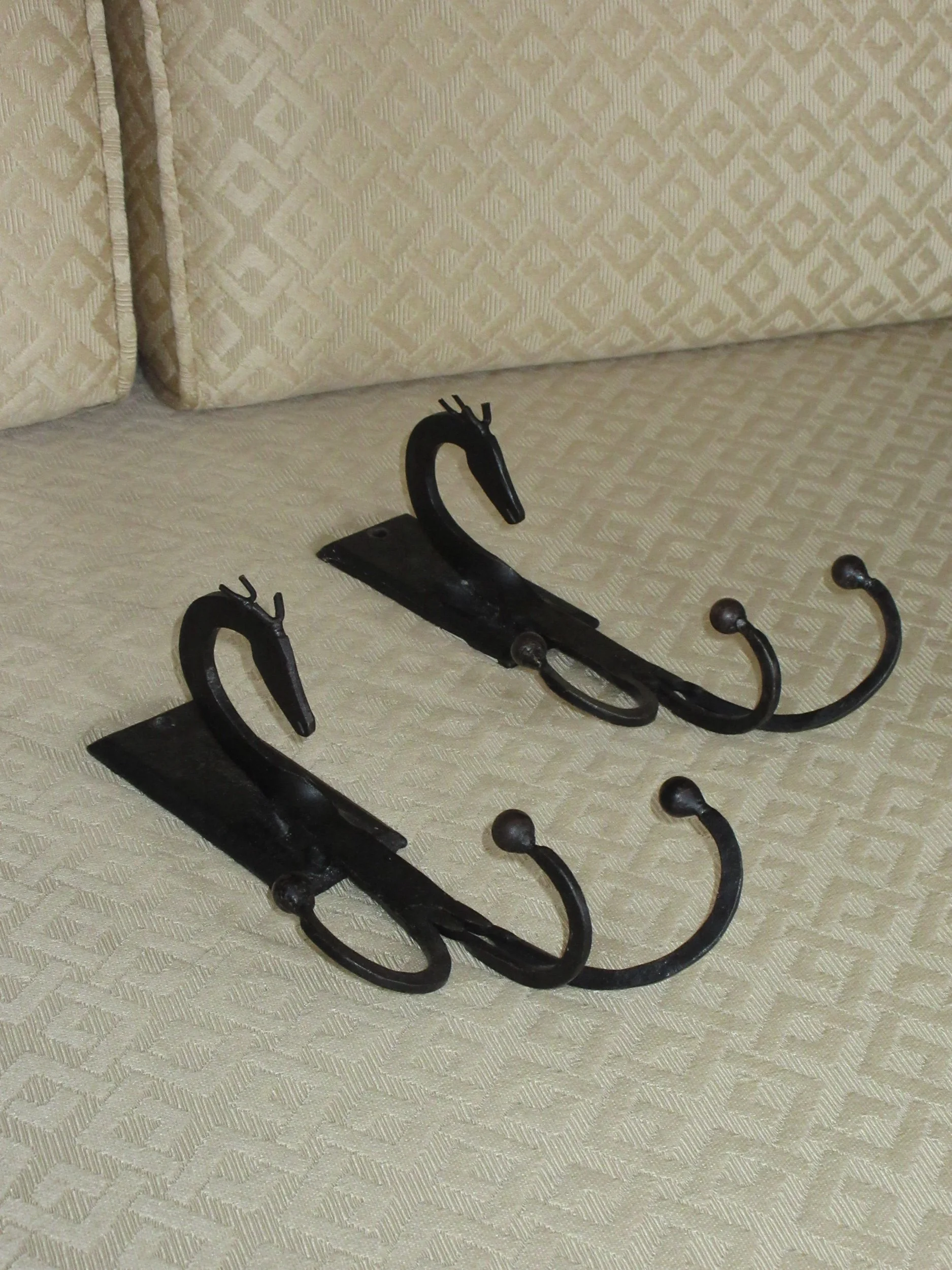 Two metal wall hooks with decorative swan designs, placed on a beige patterned fabric surface.