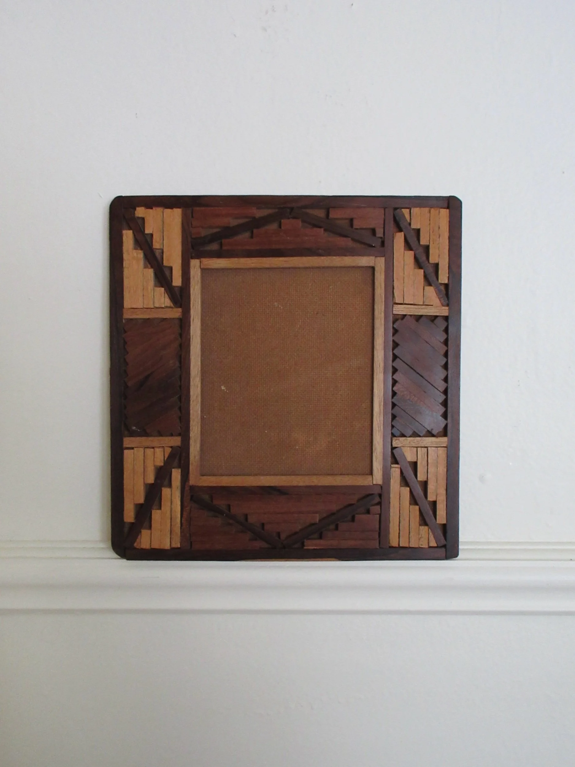 A decorative wooden picture frame with a woven design, hanging on a plain white wall.