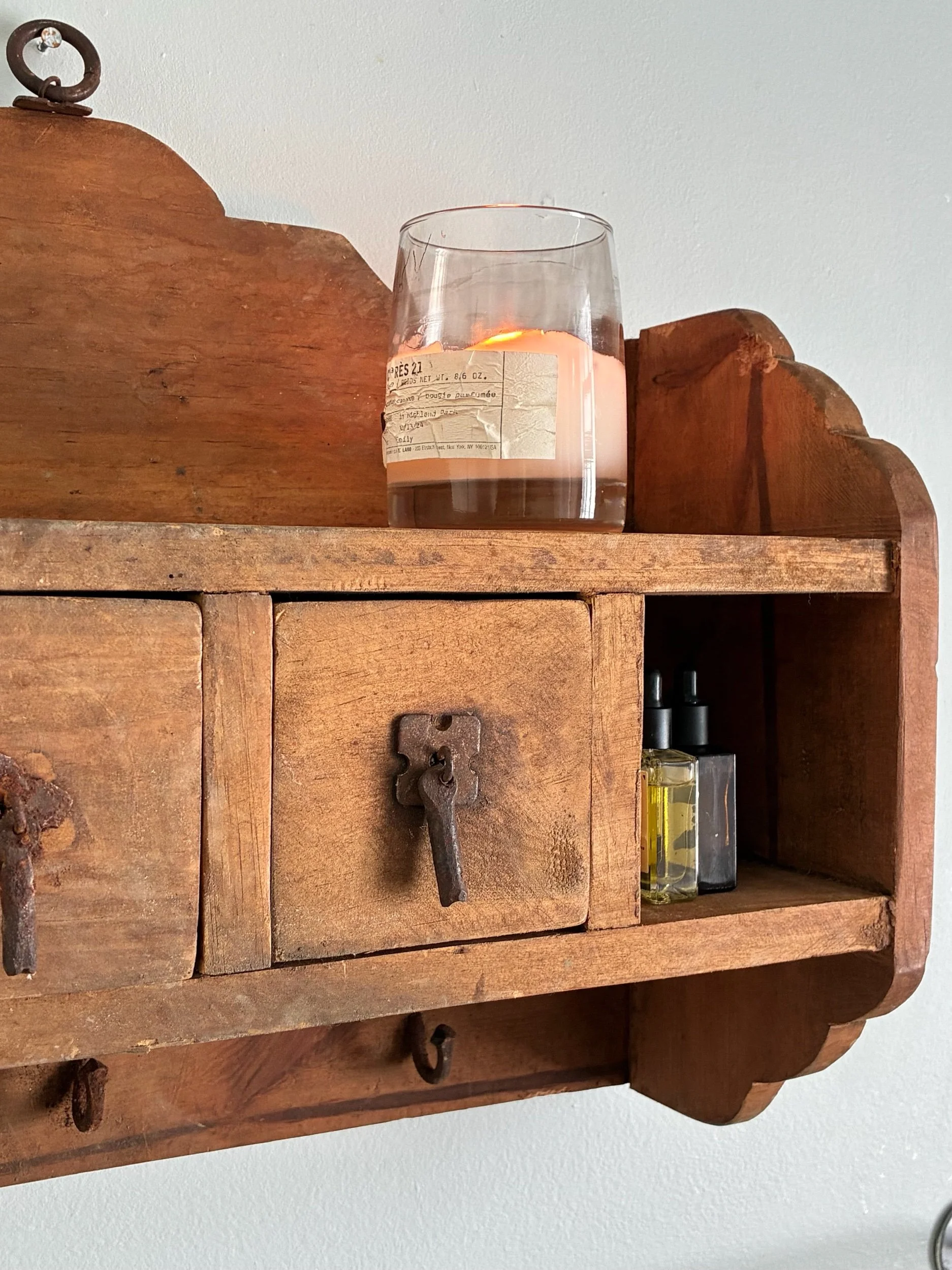 A wooden wall shelf with a large candle, glass bottles of essential oils, and vintage keys.