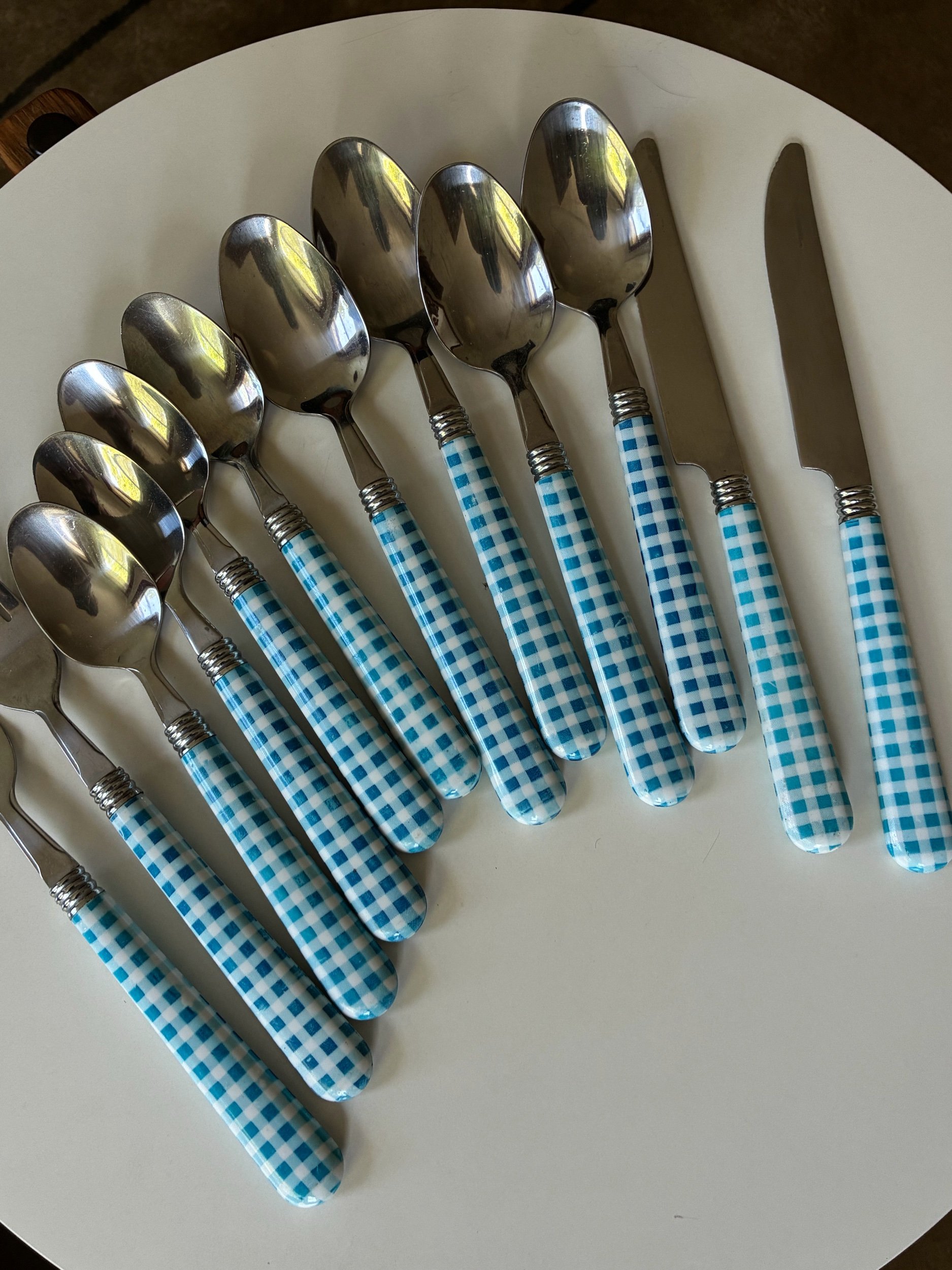 A white round tray holding eight metal spoons with blue and white checkered handles, placed in a slight curve.