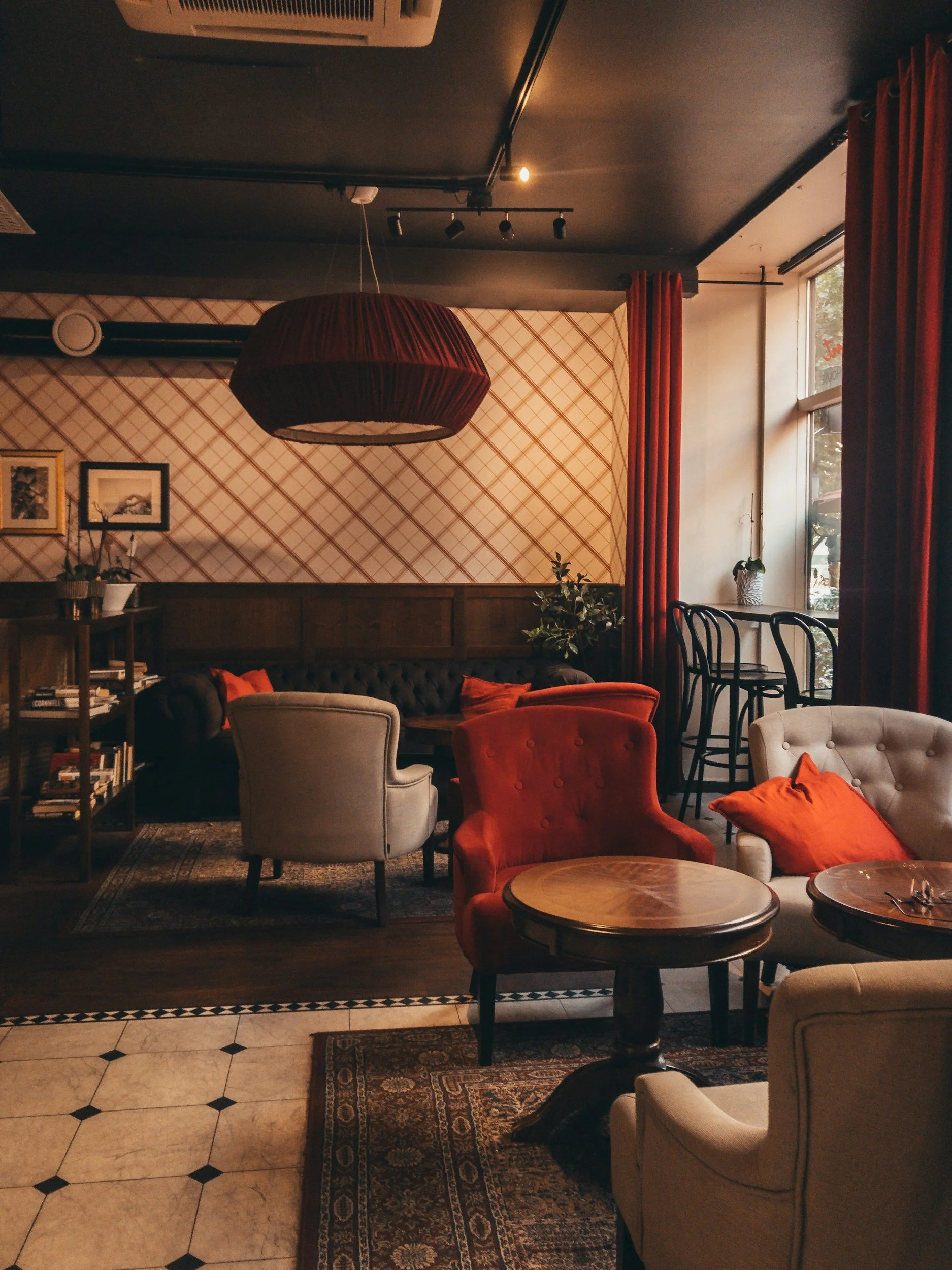 Cozy lounge area with vintage-style chairs, red curtains, and framed artwork on the wall, illuminated by warm ambient lighting.