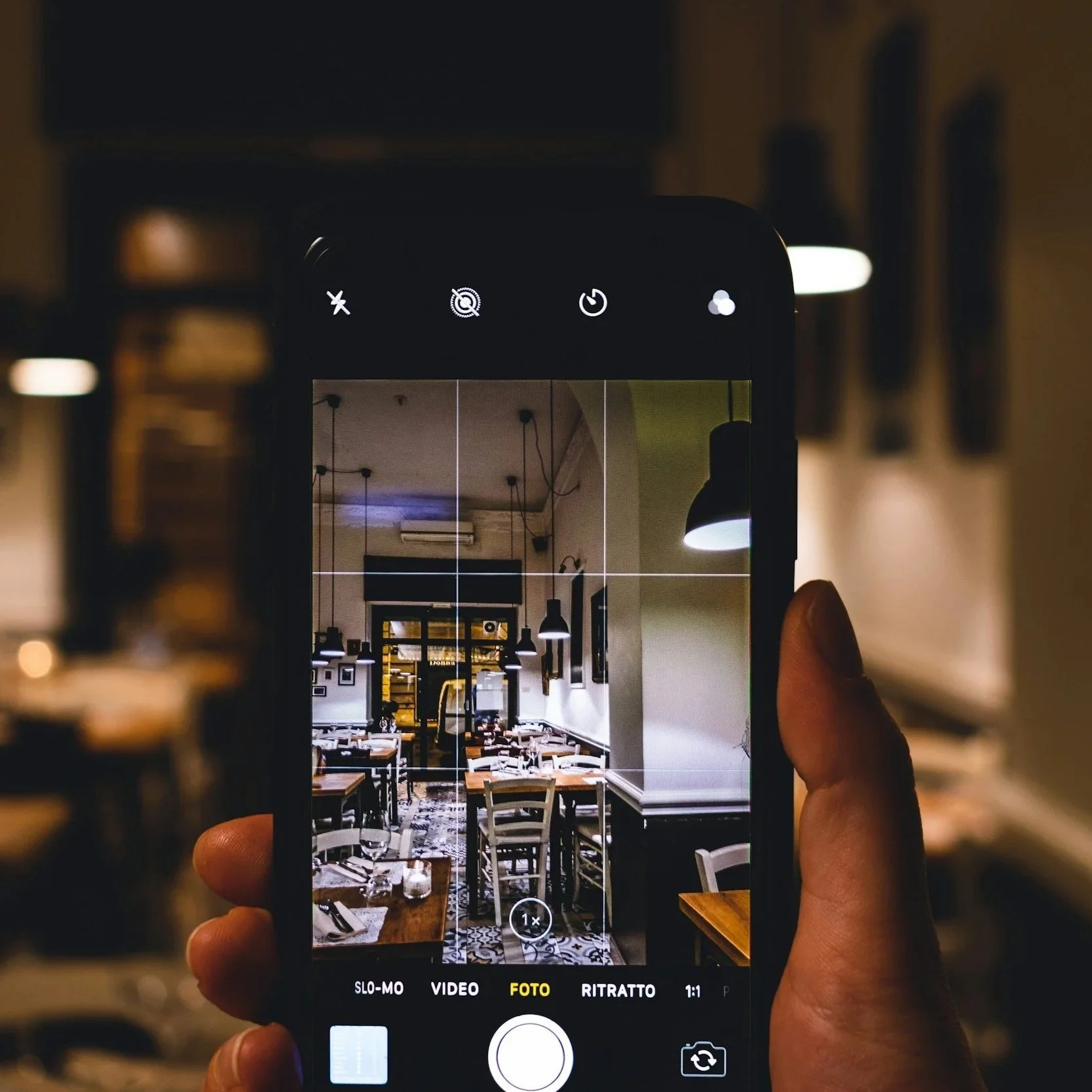 Photo of a smartphone camera screen capturing the interior of a stylish restaurant with tables, chairs, and hanging pendant lights.