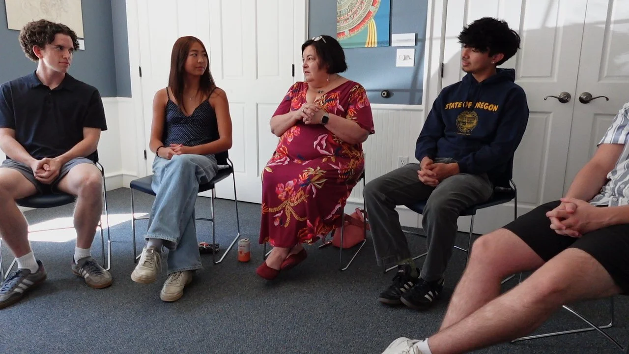 Group of five people seated in a circle during discussion in a room.