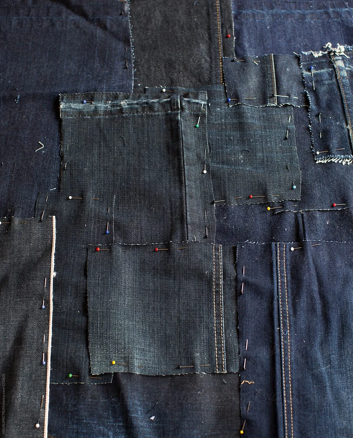 Close-up of several denim fabric patches pinned together with straight pins, likely in the process of sewing or patching.