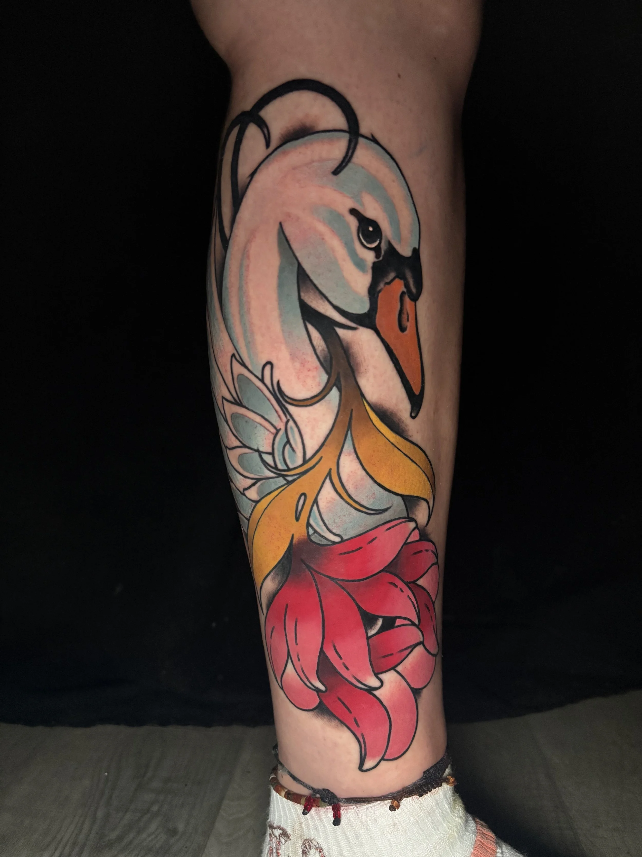 Tattoo of a swan's head with a red flower on its neck on a person's leg.