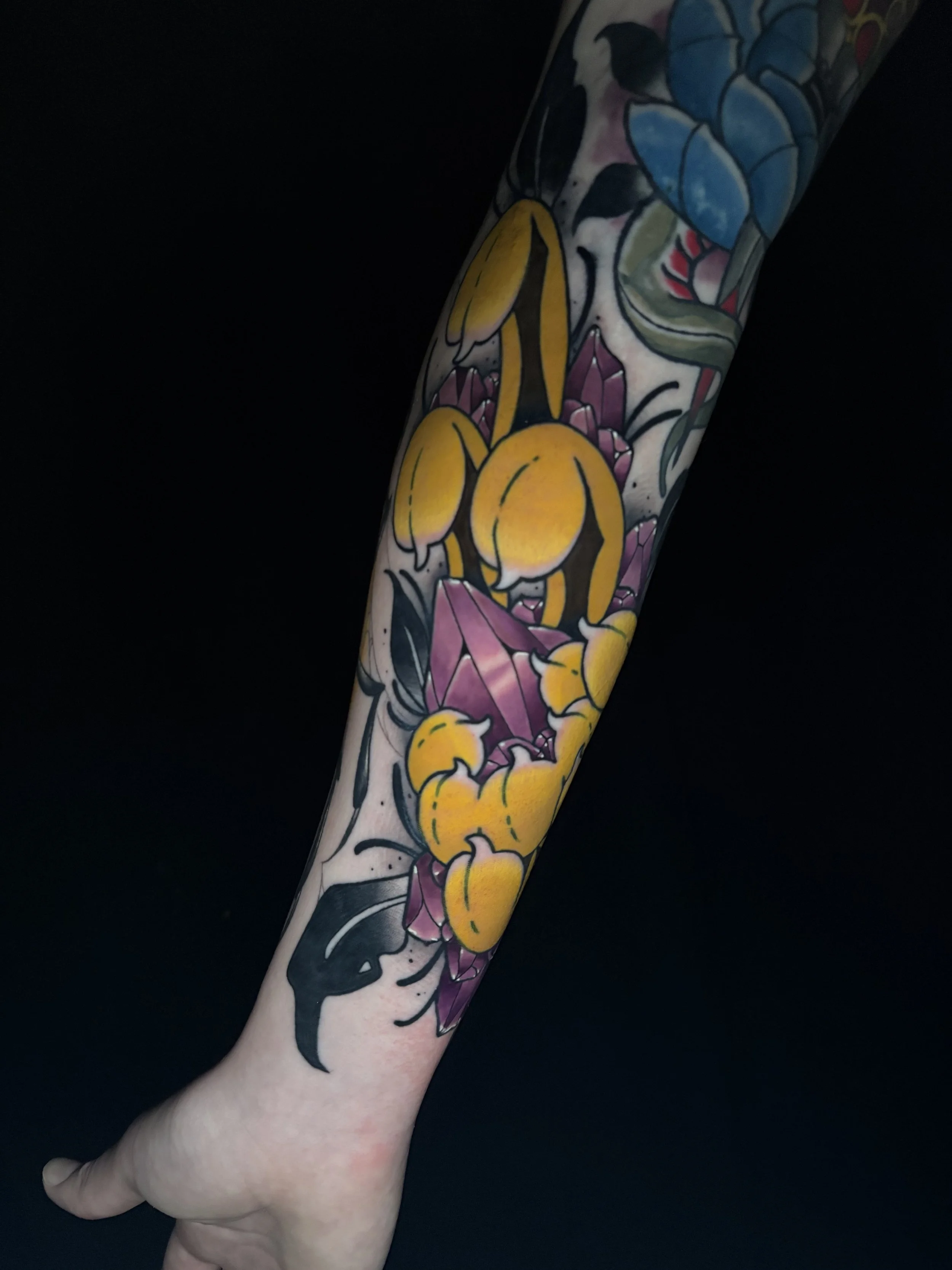 Colorful tattoo on person's arm featuring yellow chrysanthemum, amethyst crystals.