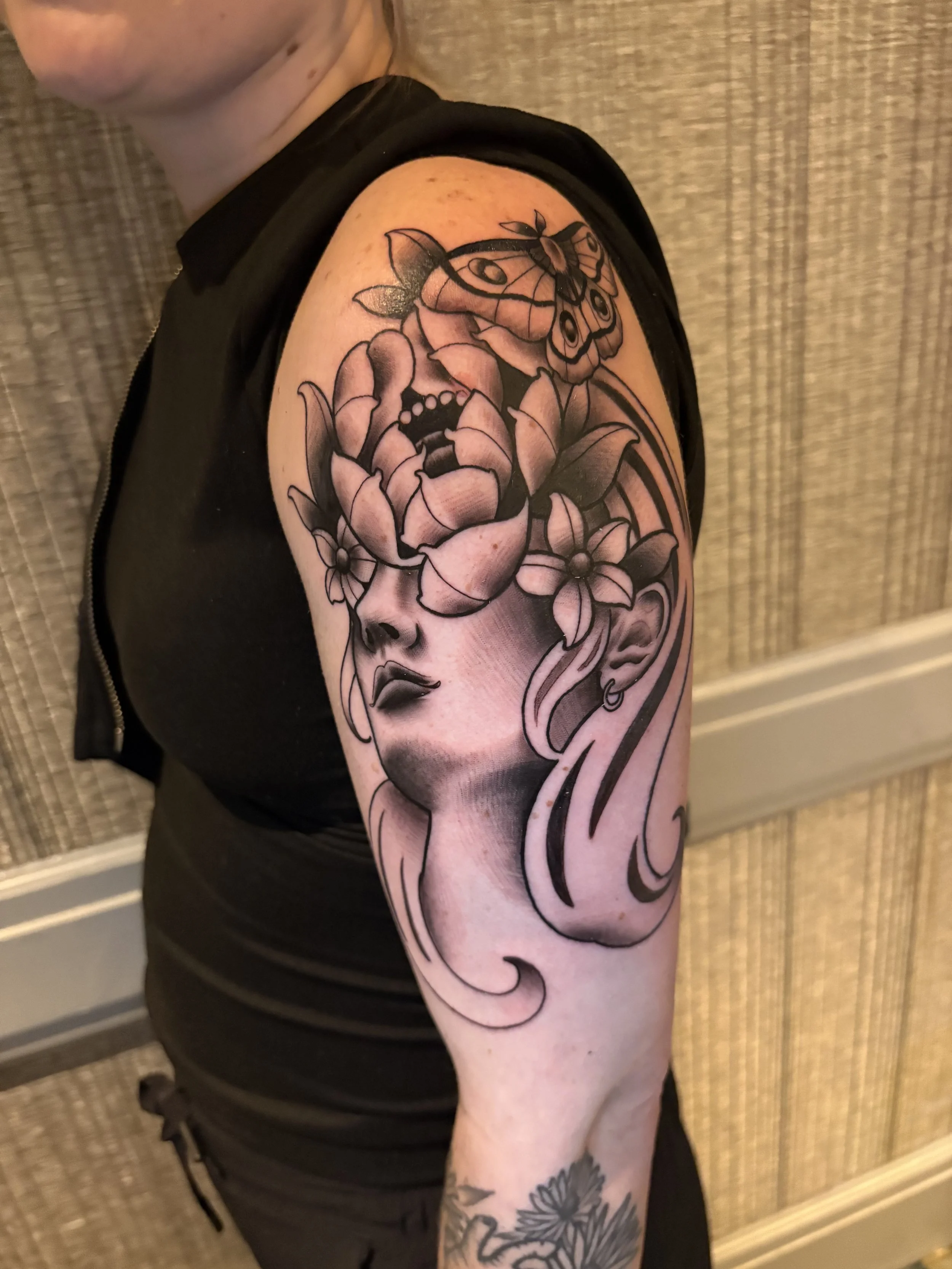 Tattoo of a woman's face with flowers and a butterfly on the shoulder.