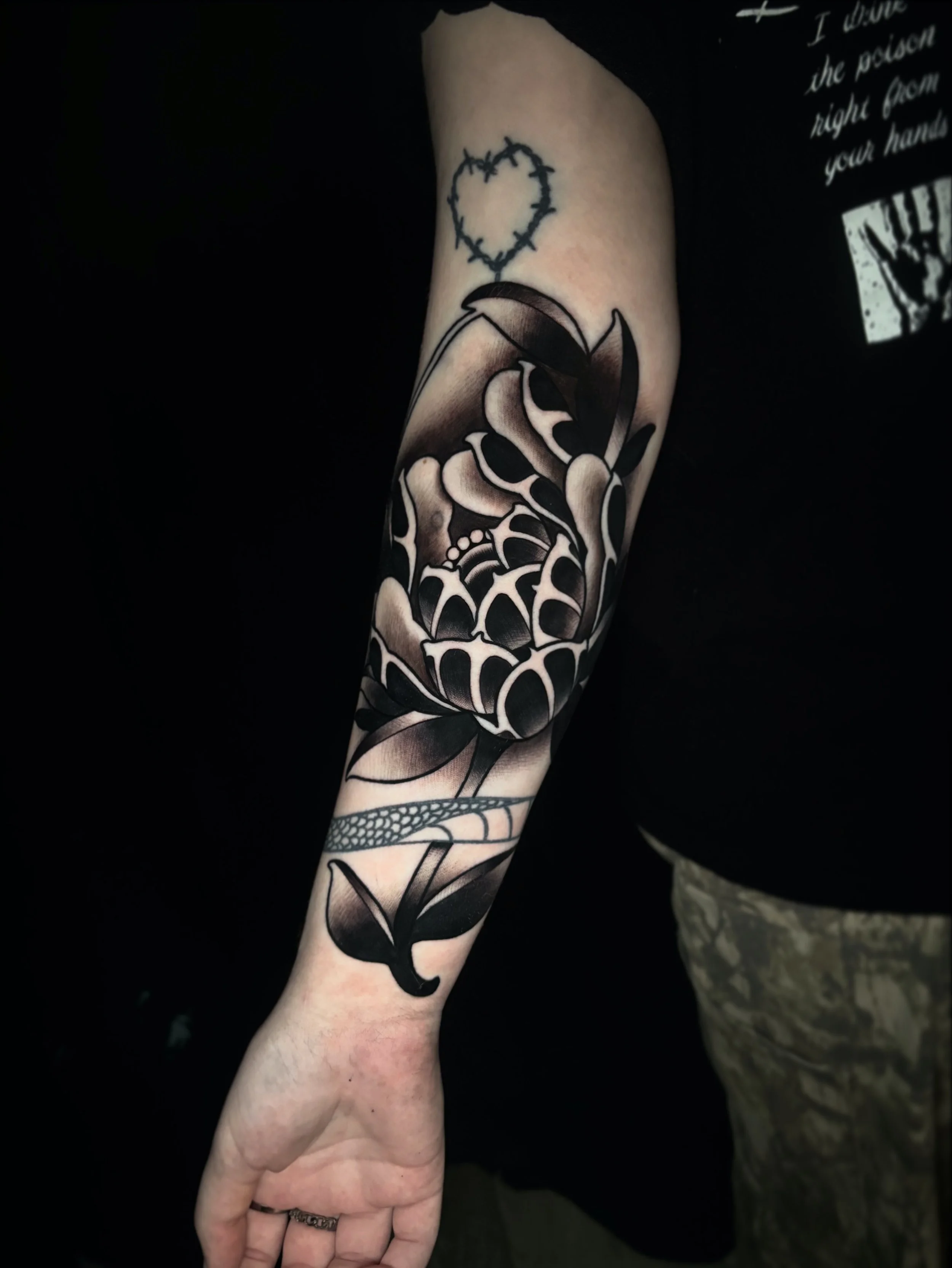 A person's arm with a tattoo of a large black and white floral peony design.