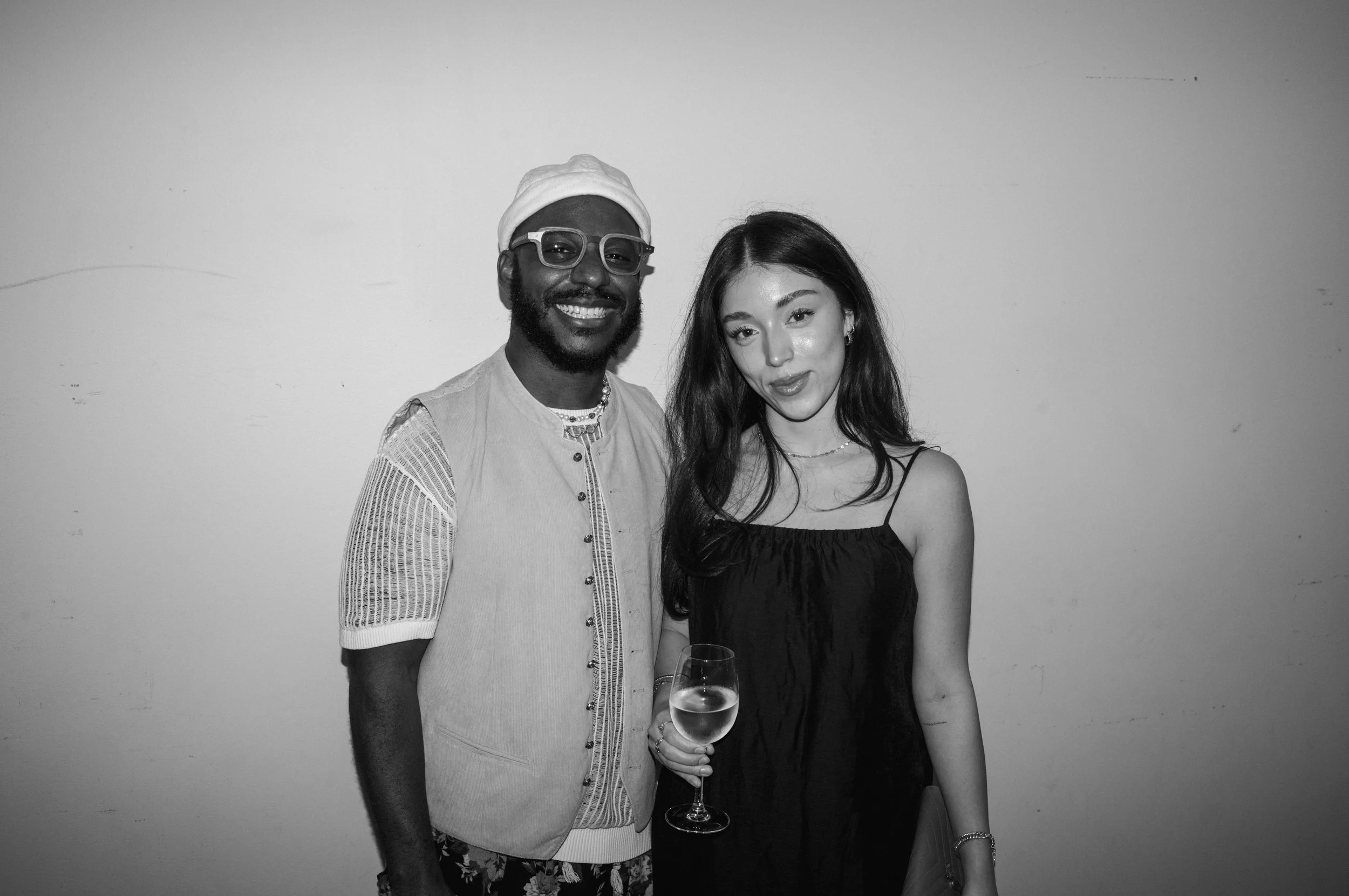 A man and a woman posing for a photo, with the woman holding a glass of white wine.