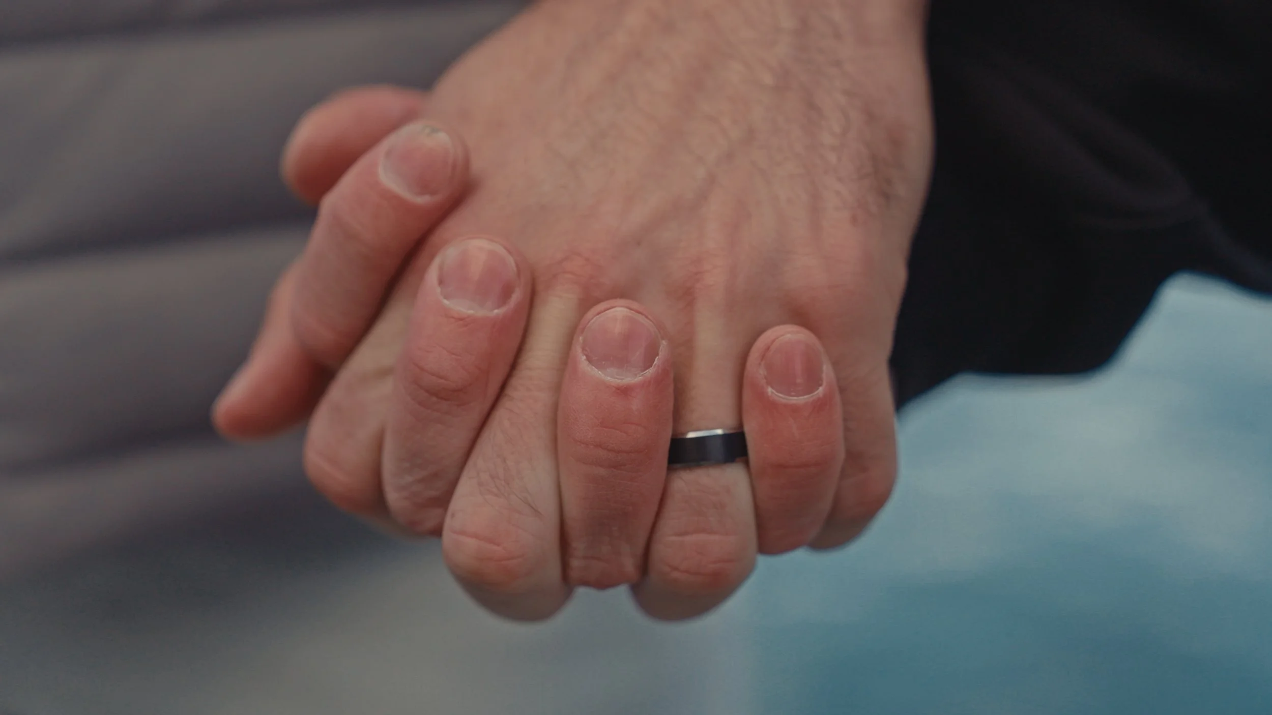 Close-up of two hands clasped together, one hand wearing a black ring, suggesting a gesture of support or unity.