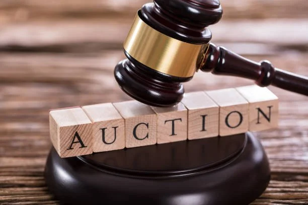 A judge's gavel resting on a wooden auction block with wooden blocks spelling 'AUCTION' in front of it.