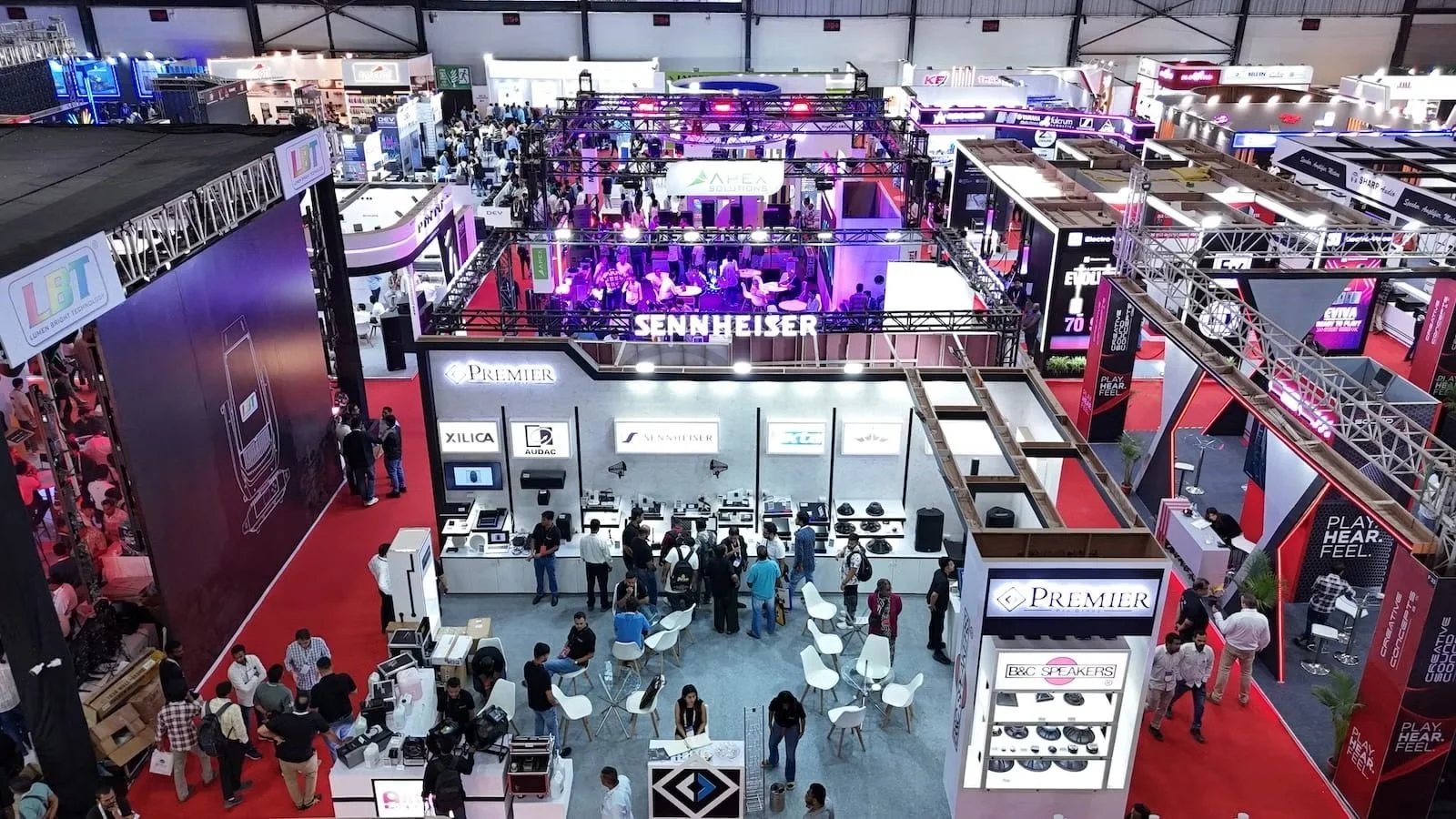 A busy exhibition hall filled with various booths showcasing electronic and audio products, with visitors walking around and interacting with displays.