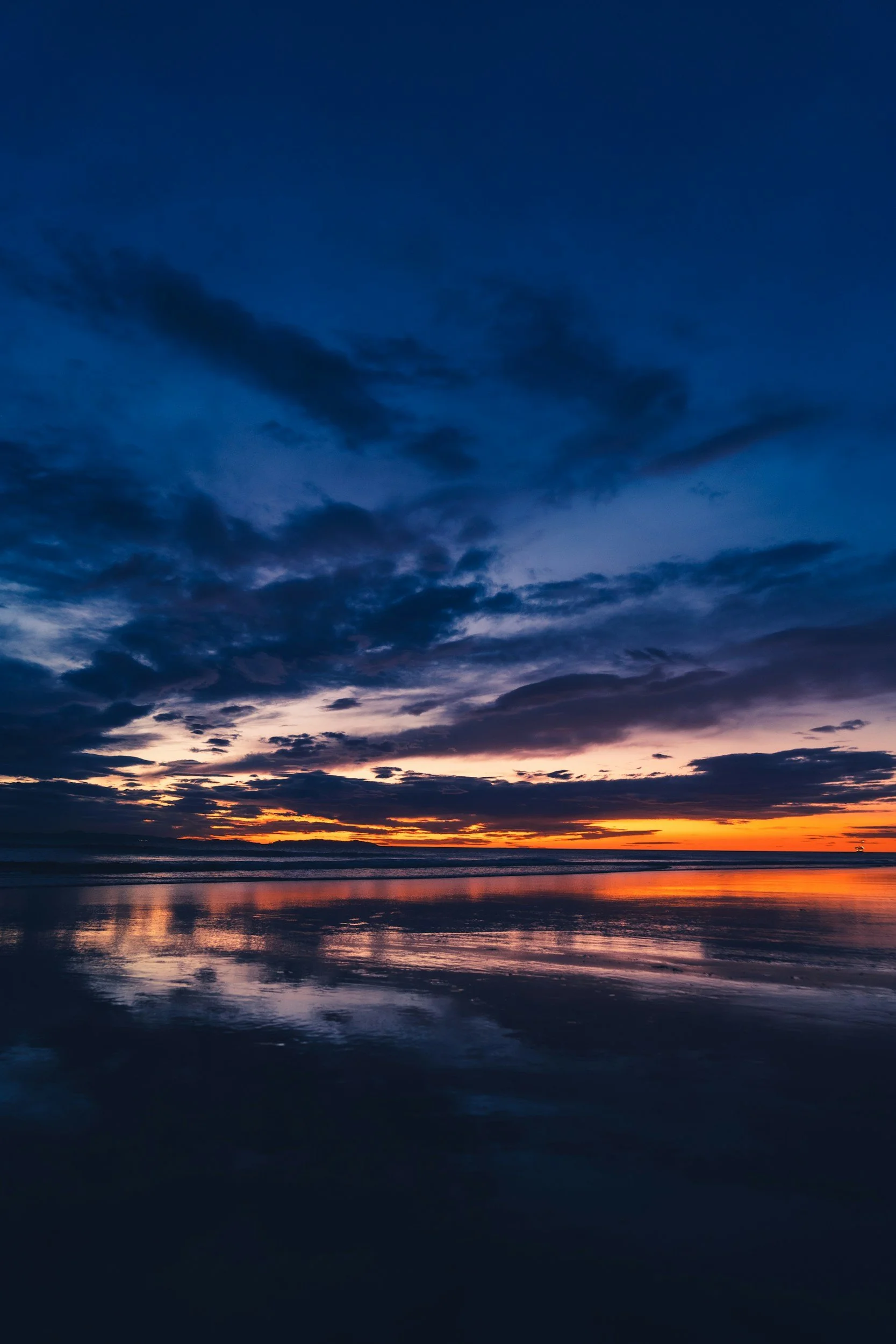 Sunset over the ocean with dark clouds, reflected on the water's surface.