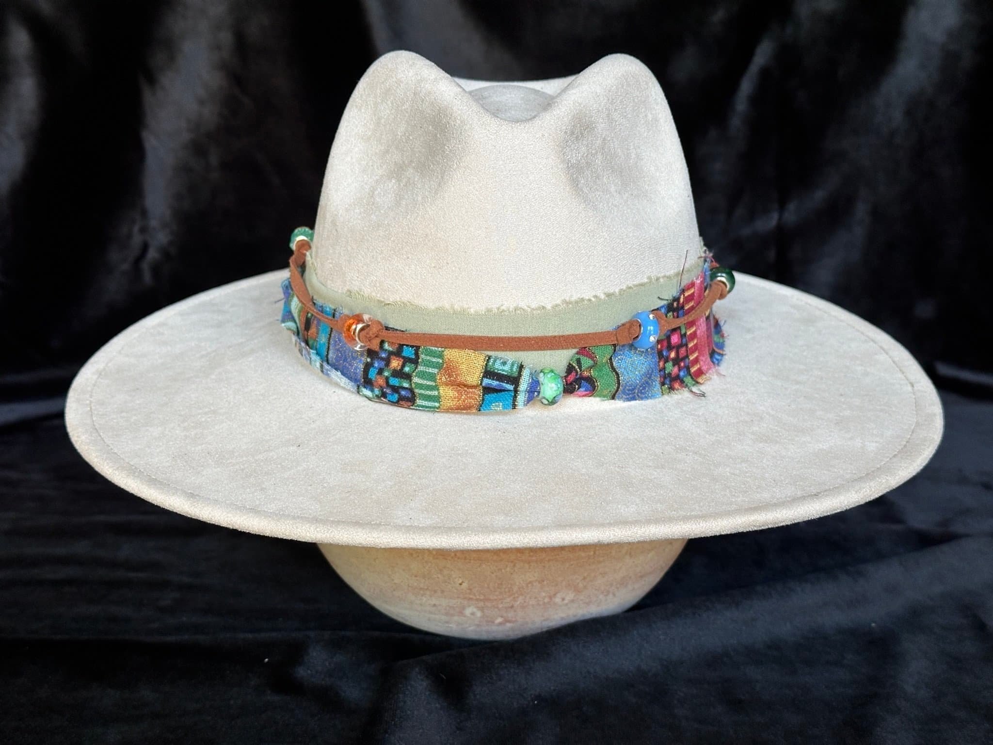 Front View Light beige felt hat with a wide brim and a colorful, patterned fabric band, set against a black background.
