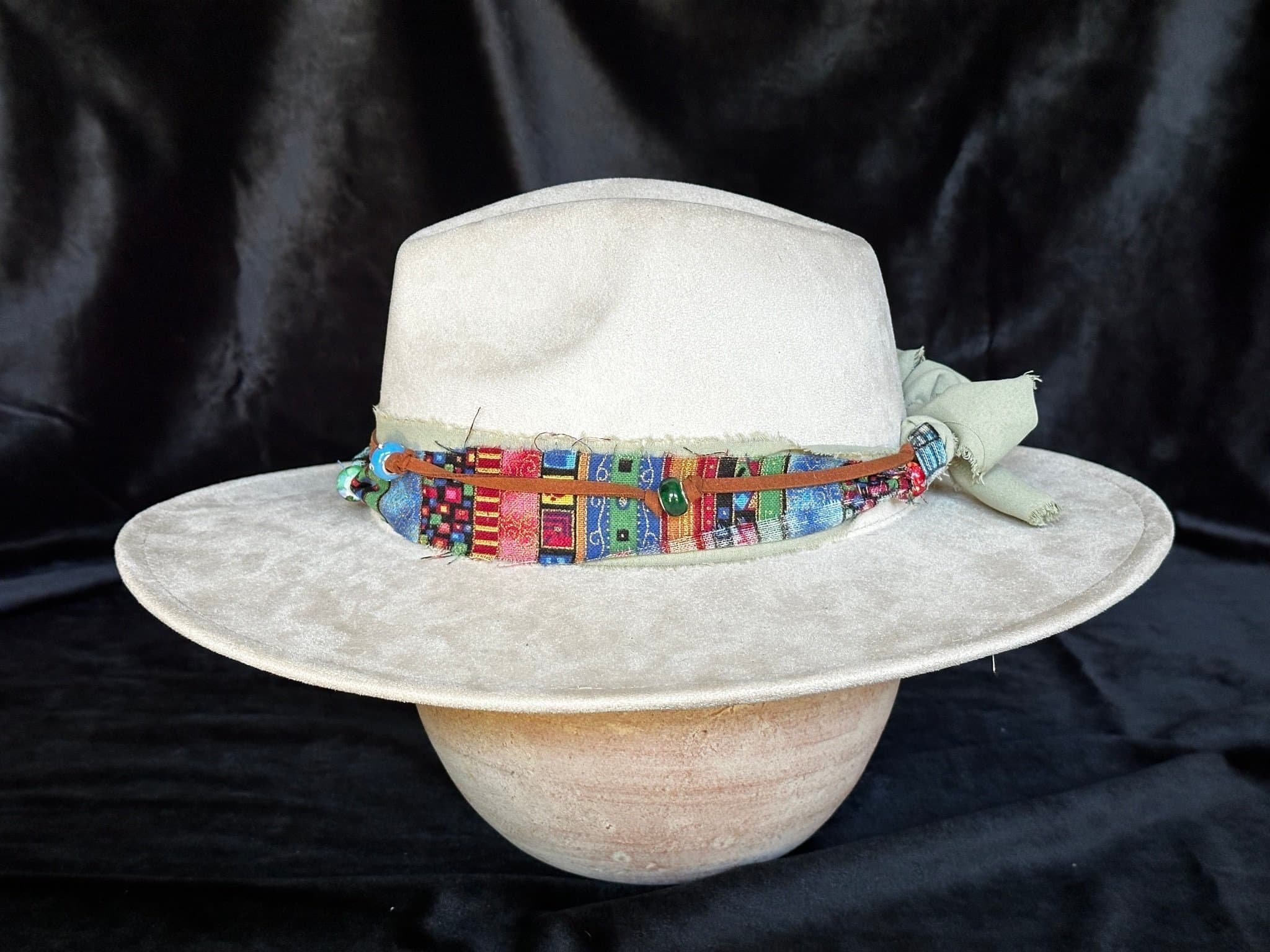Side View Light beige felt hat with a wide brim and a colorful, patterned fabric band, set against a black background.