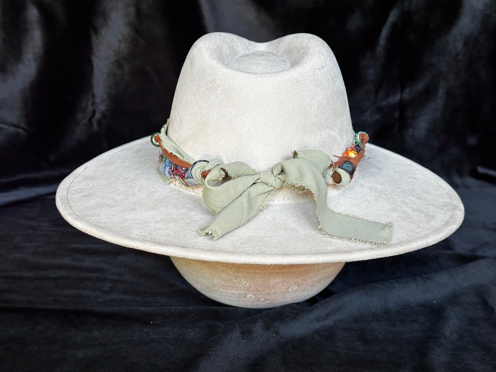 Back View Light beige felt hat with a wide brim and a colorful, patterned fabric band, set against a black background.