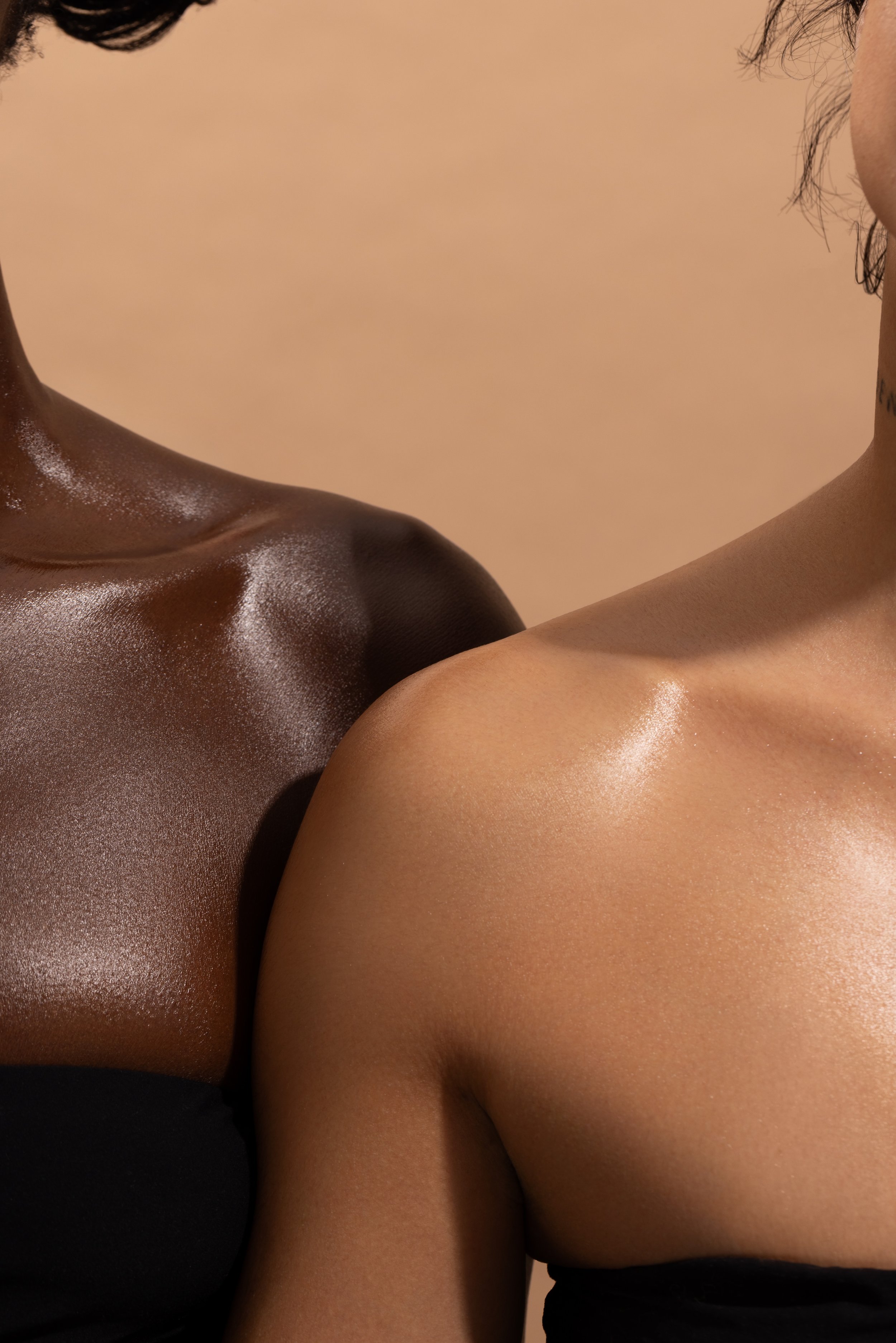 Close-up image of two people's shoulders and necks, one with dark skin and the other with light skin, glowing skin.