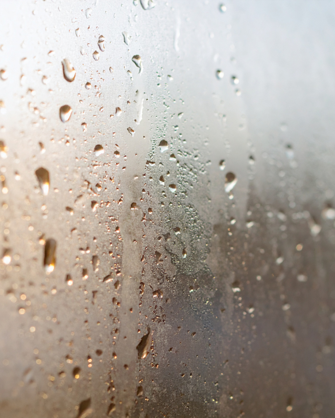 Close-up of a foggy or steamy window with water droplets on the surface.