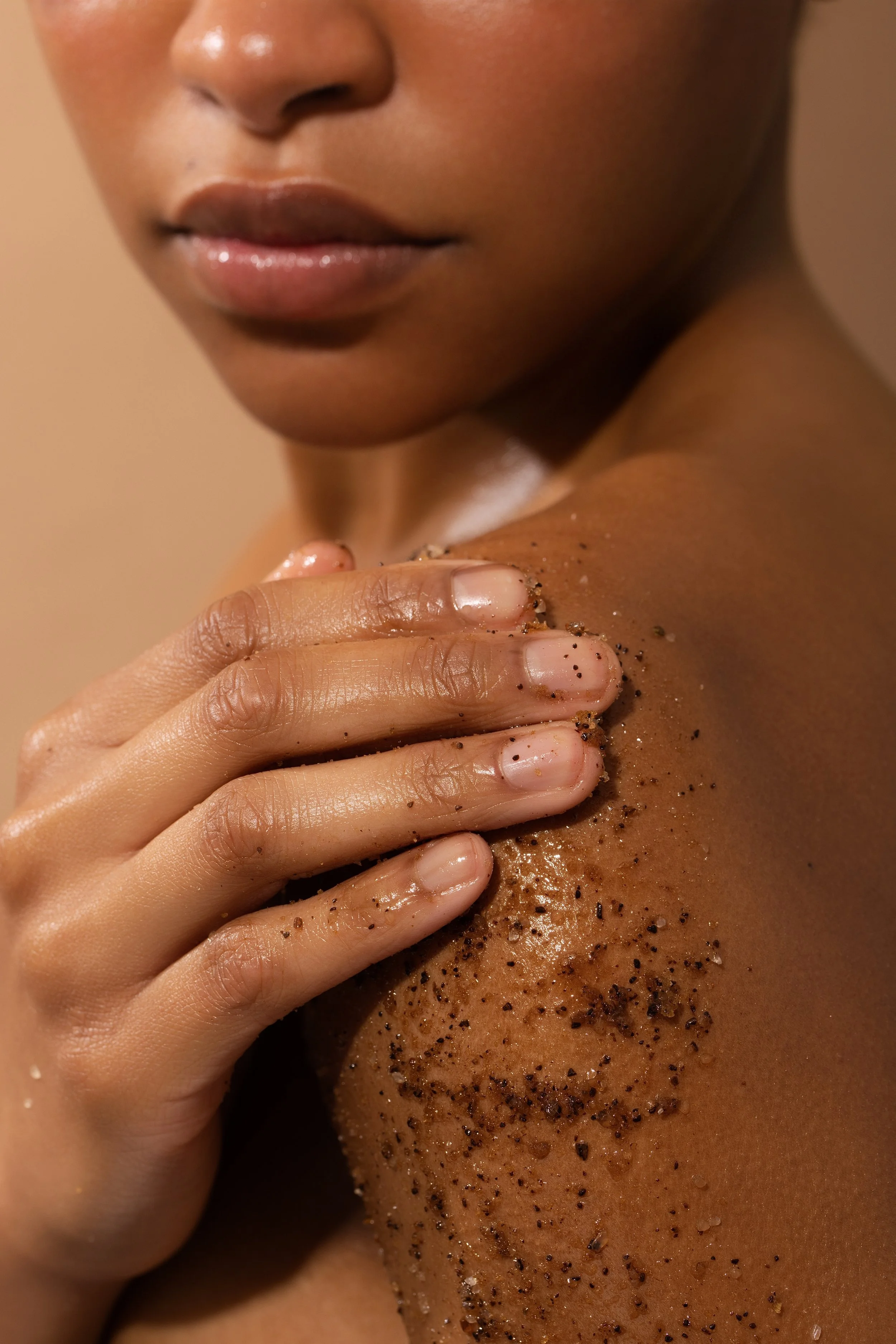 Close-up of a person with a dark complexion, touching their shoulder, covered in A2 coffee body polish.