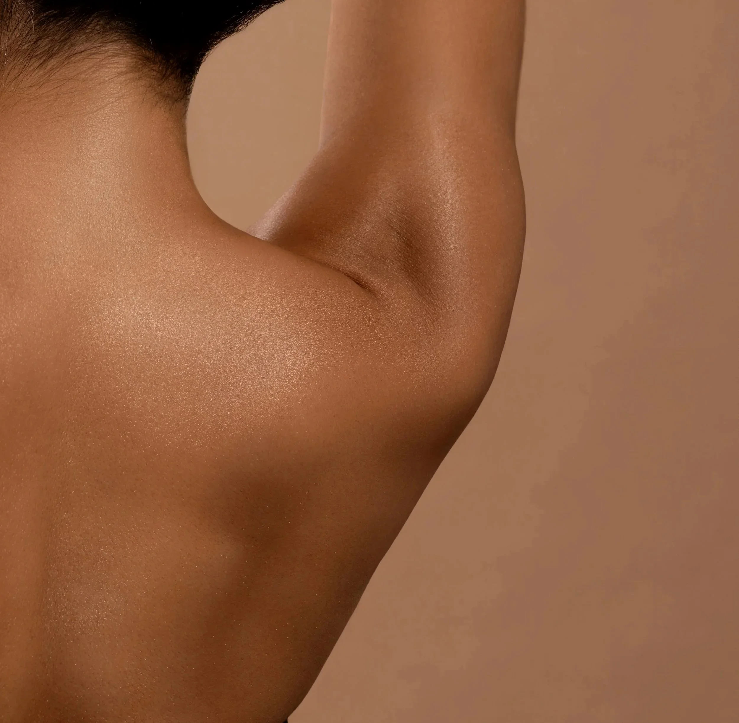 Close-up of a person's arm and shoulder with smooth skin and a warm brown tone against a beige background.