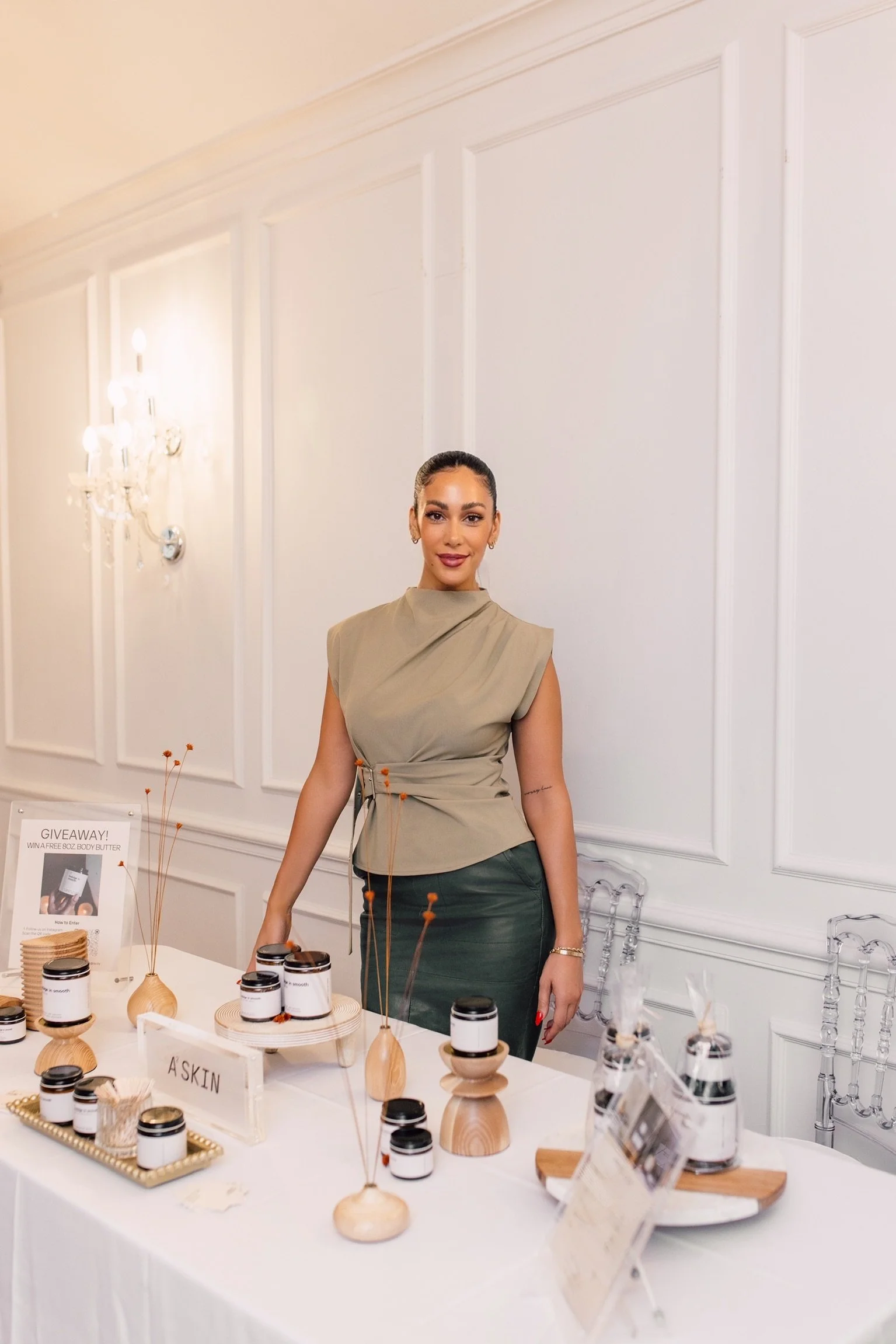A woman standing behind a table with skincare products. Natural, A2, Andria Corradetti